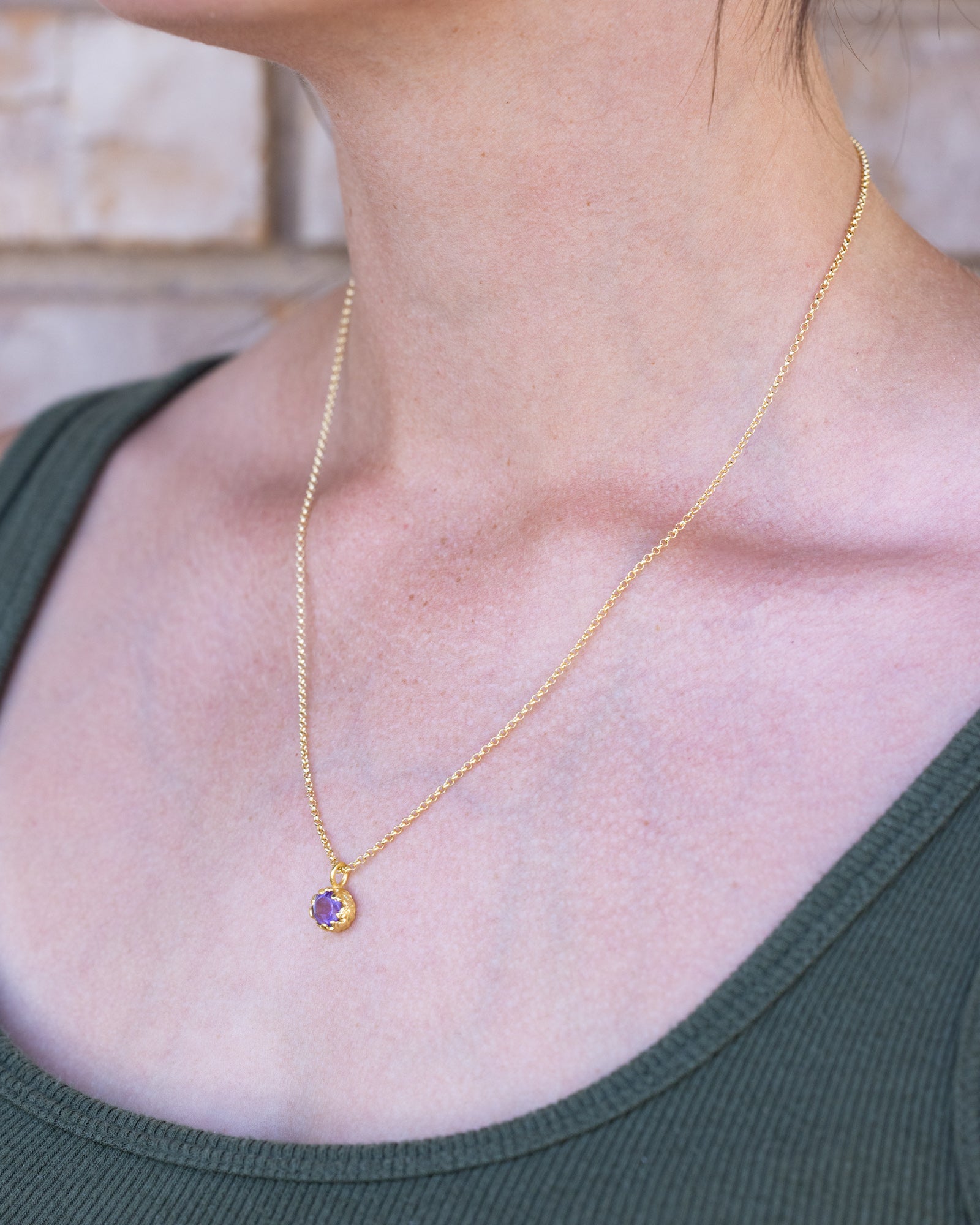 Gold necklace with a purple amethyst on a person wearing a green top.