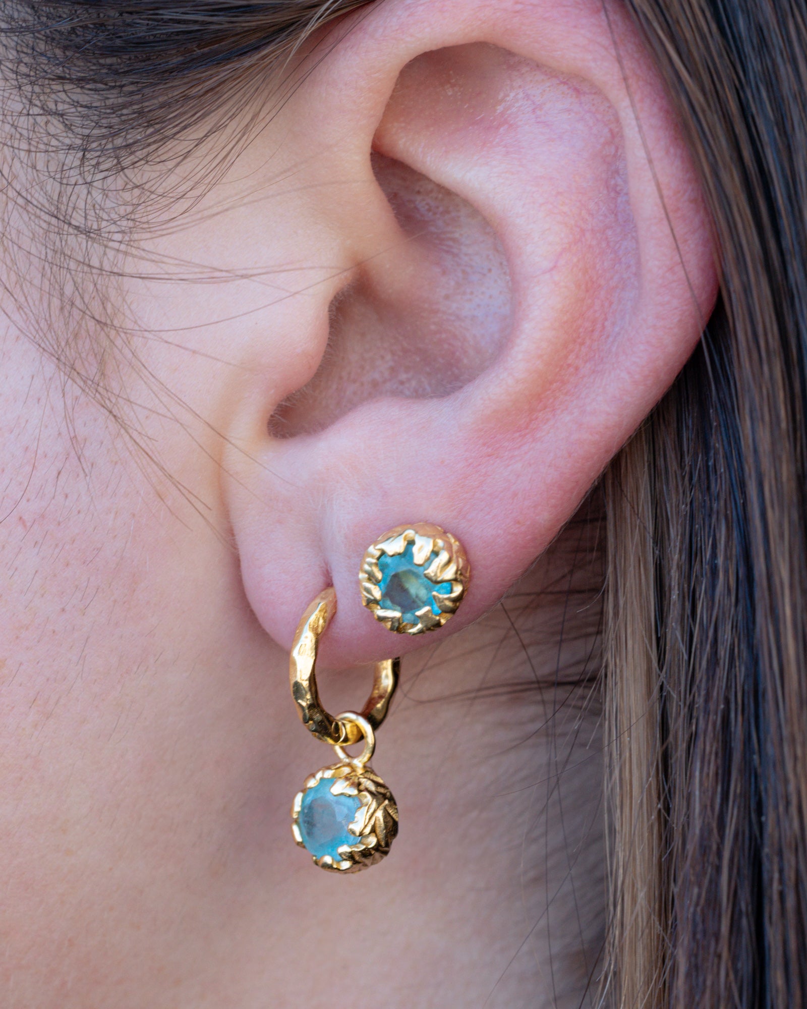Close-up of an ear wearing gold earrings with blue aquamarine.