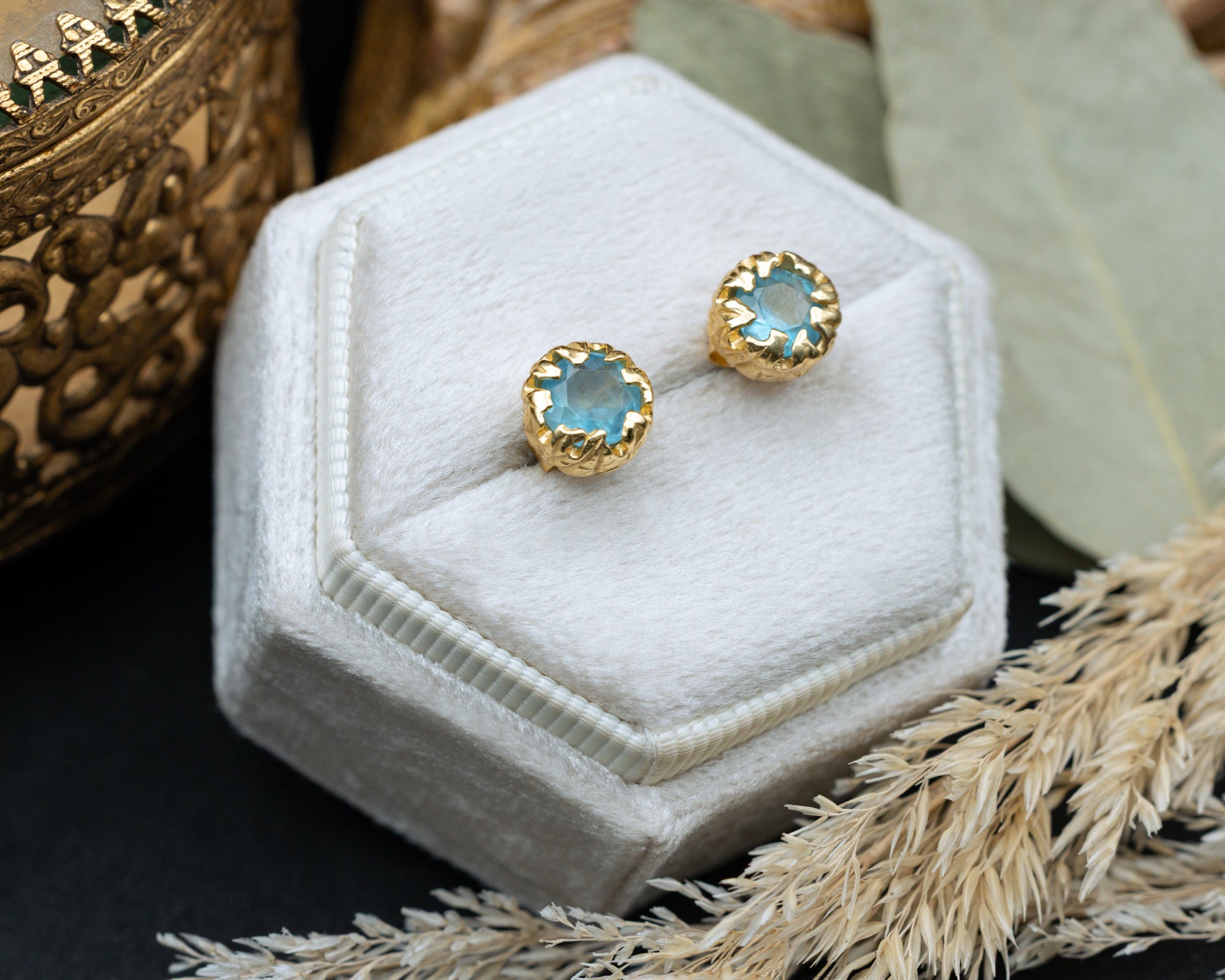 Gold earrings with blue aquamarine on a white hexagonal jewelry display box.