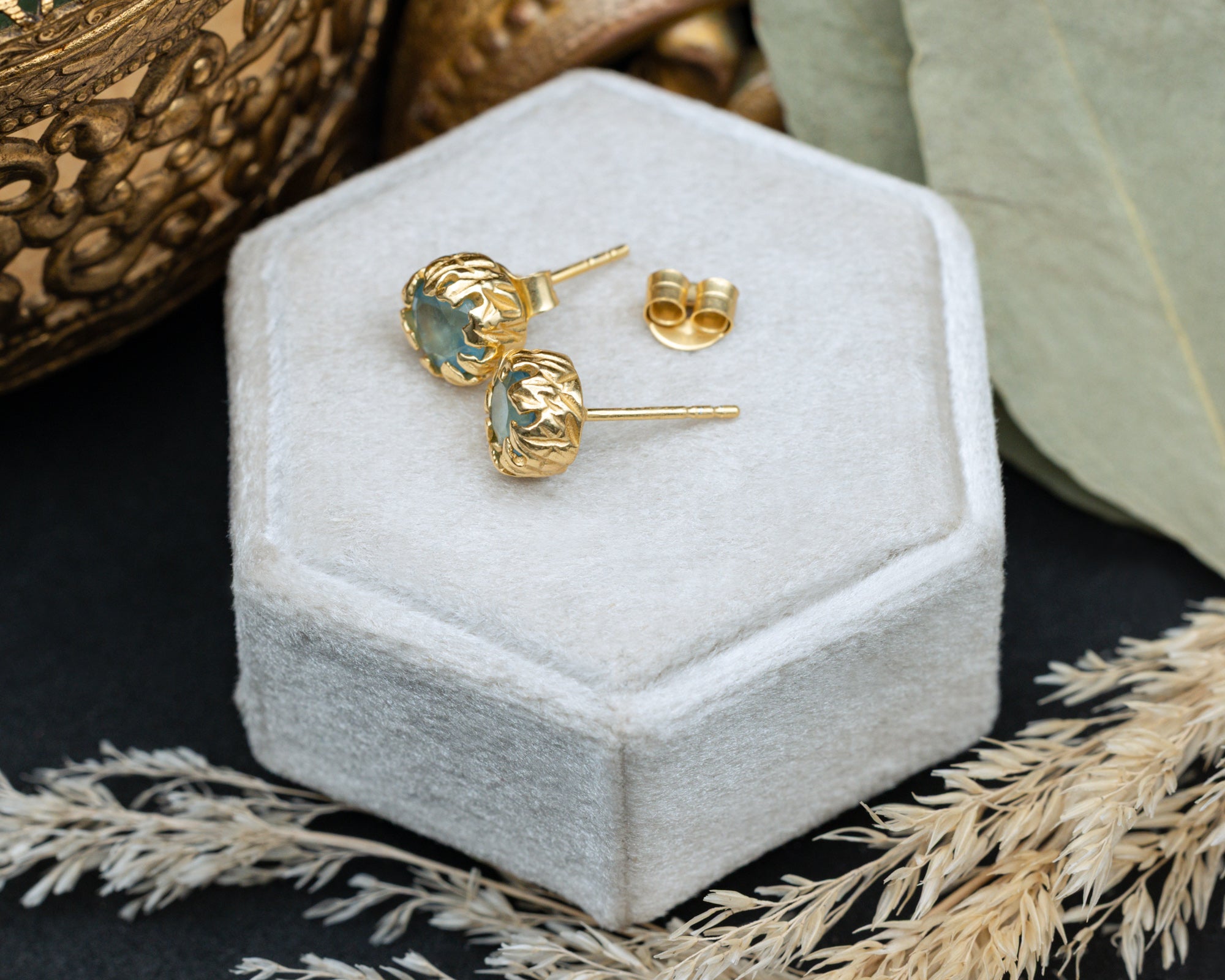 Gold aquamarine earrings on a white jewelry box with decorative elements