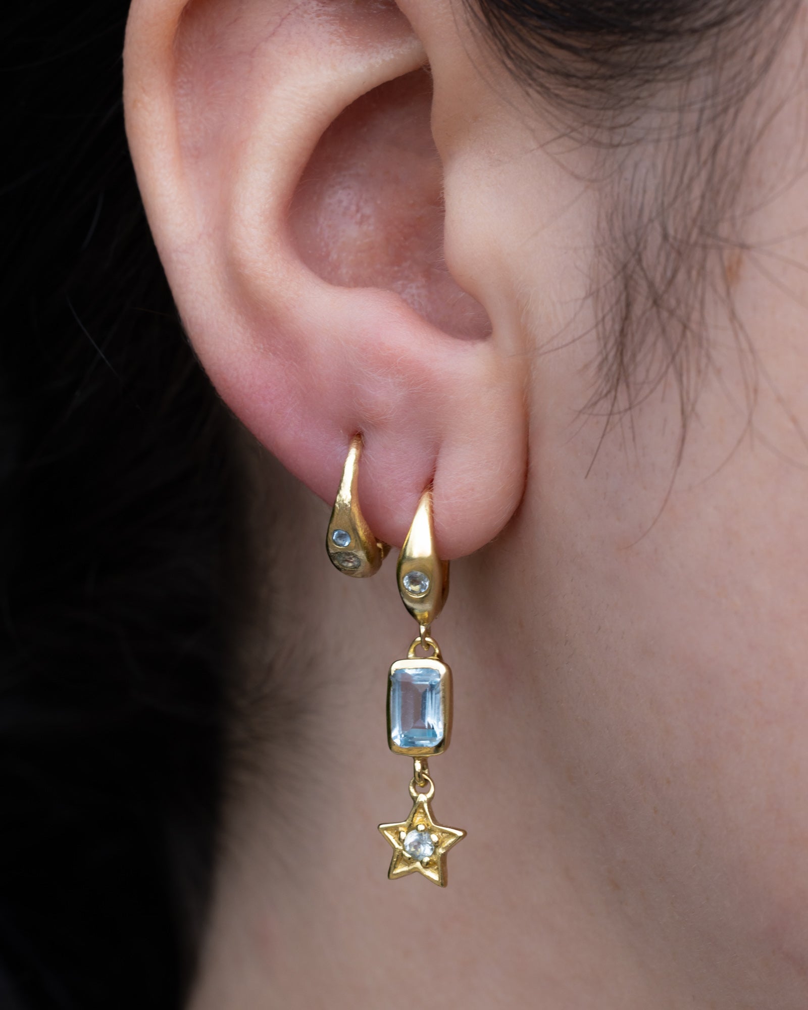Gold earrings with blue topaz accents worn by a person