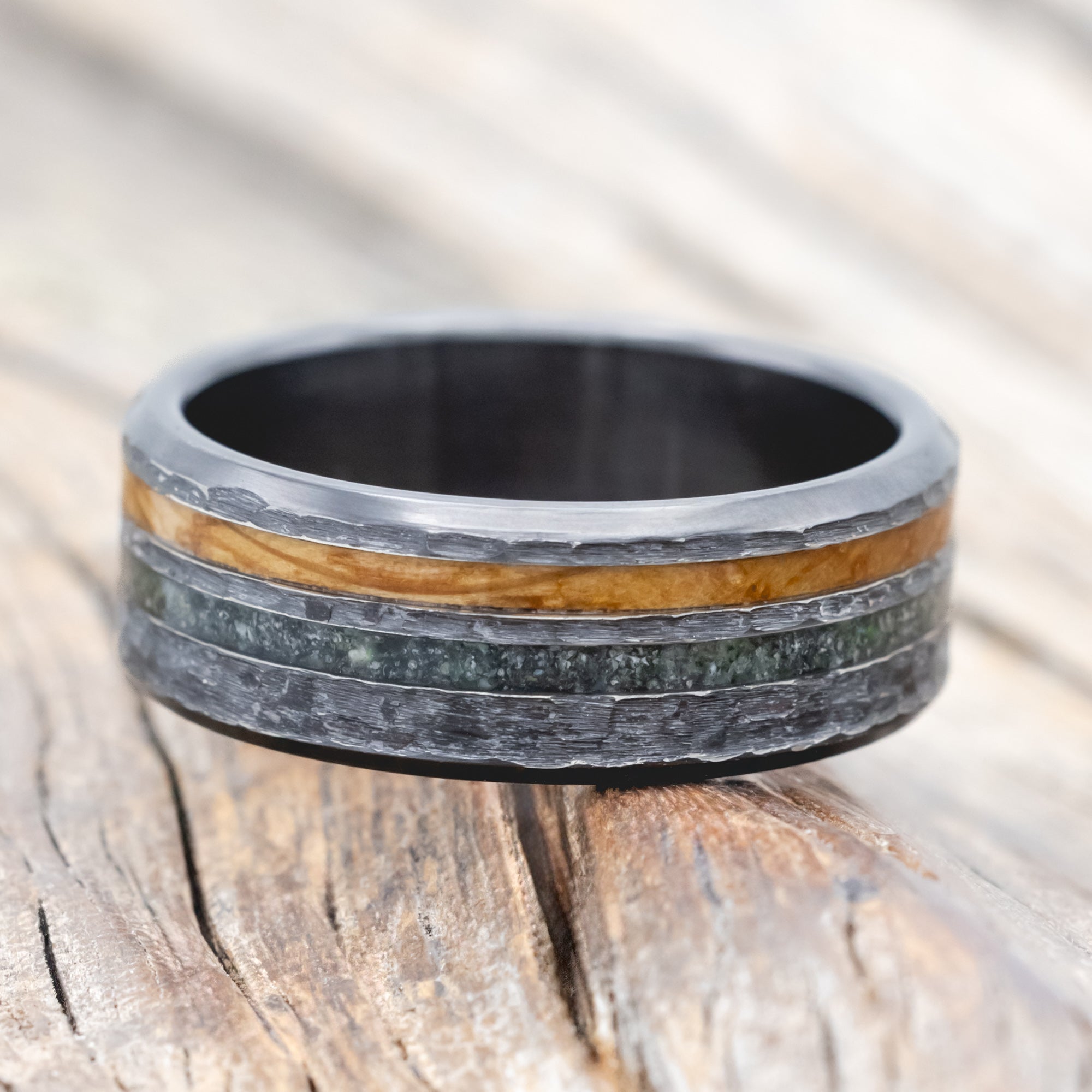 Black zirconium ring with whiskey barrel oak and moss agate on a wooden surface