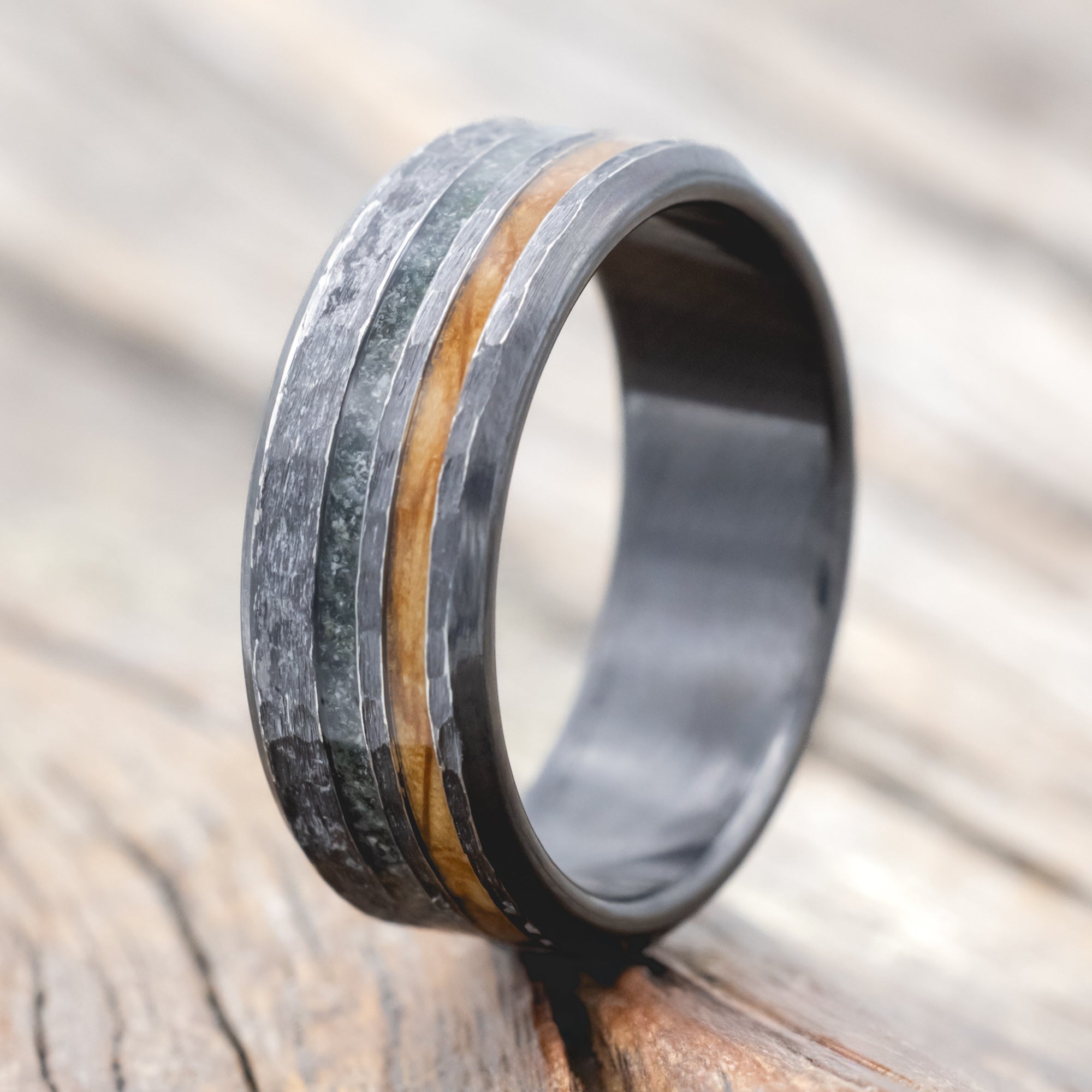Black zirconium ring with whiskey barrel oak and moss agate on a wooden surface