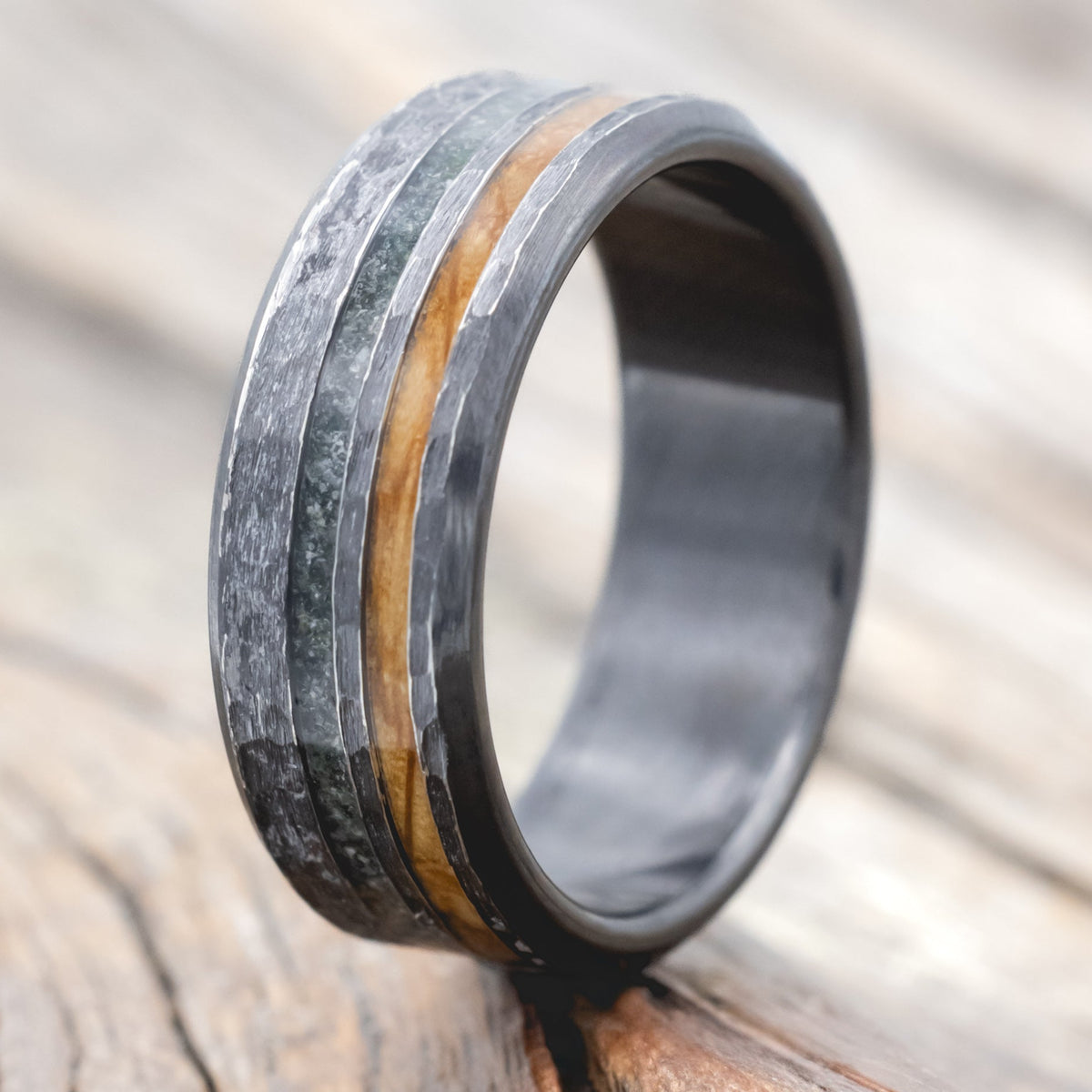 Black zirconium ring with whiskey barrel oak and moss agate on a wooden surface