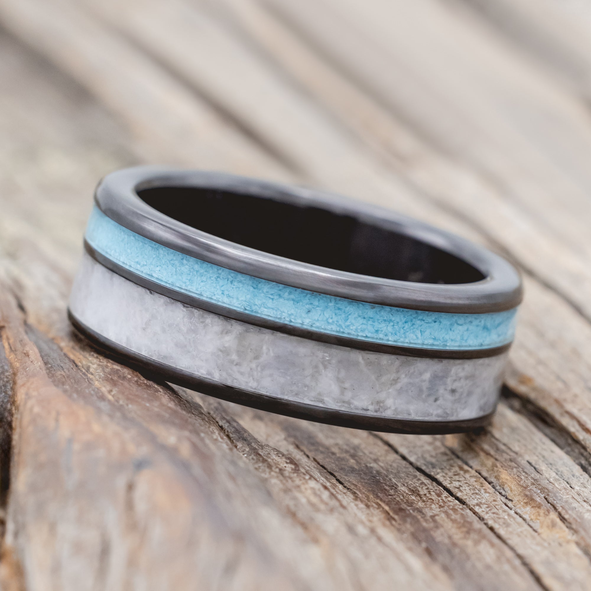 Black zirconium ring with turquoise and custom wedding dress inlays on a wooden surface