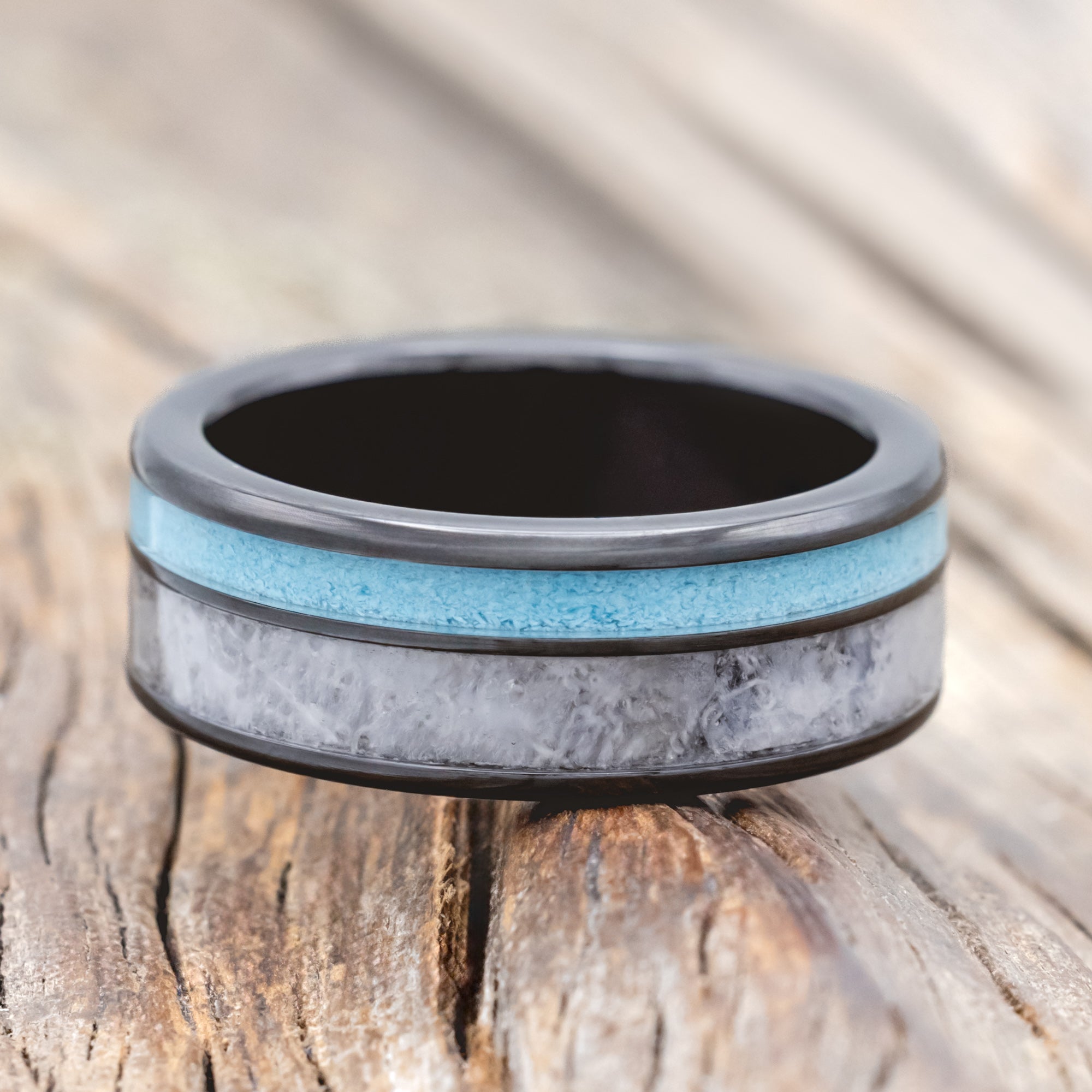 Black zirconium ring with turquoise and custom wedding dress inlays on a wooden surface
