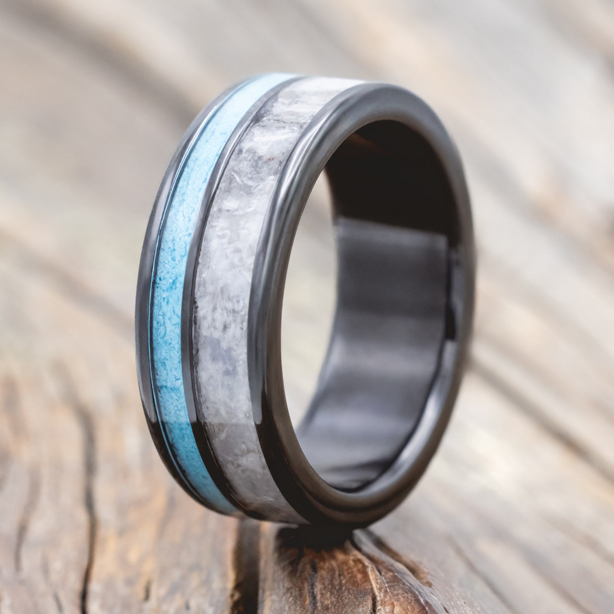 Black zirconium ring with turquoise and custom wedding dress inlays on a wooden surface