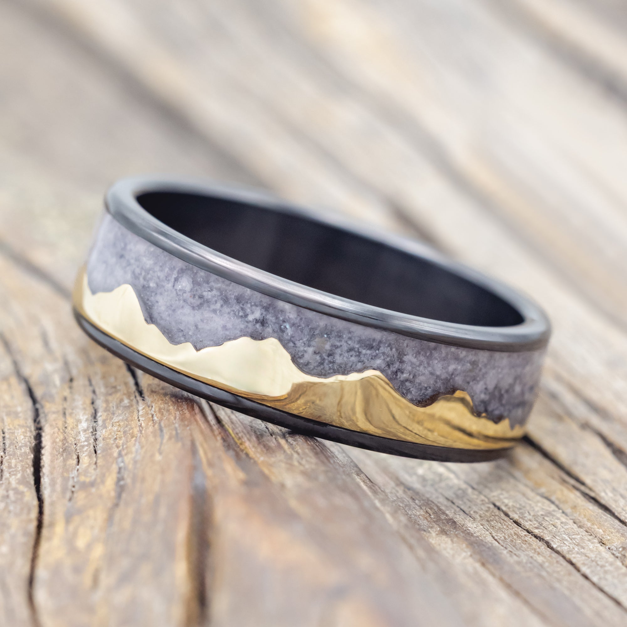 Black zirconium ring with 14K gold mountain design on a wooden surface