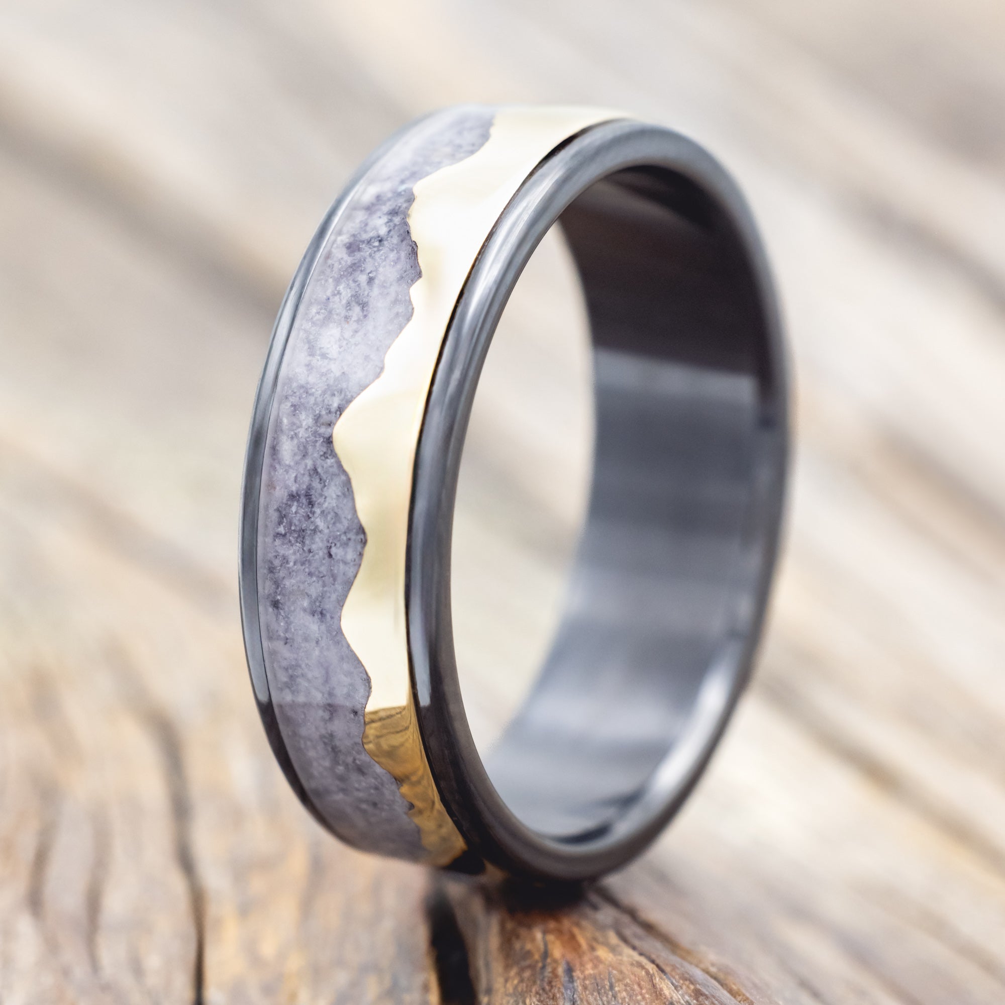 Black zirconium ring with 14K gold mountain design on a wooden surface