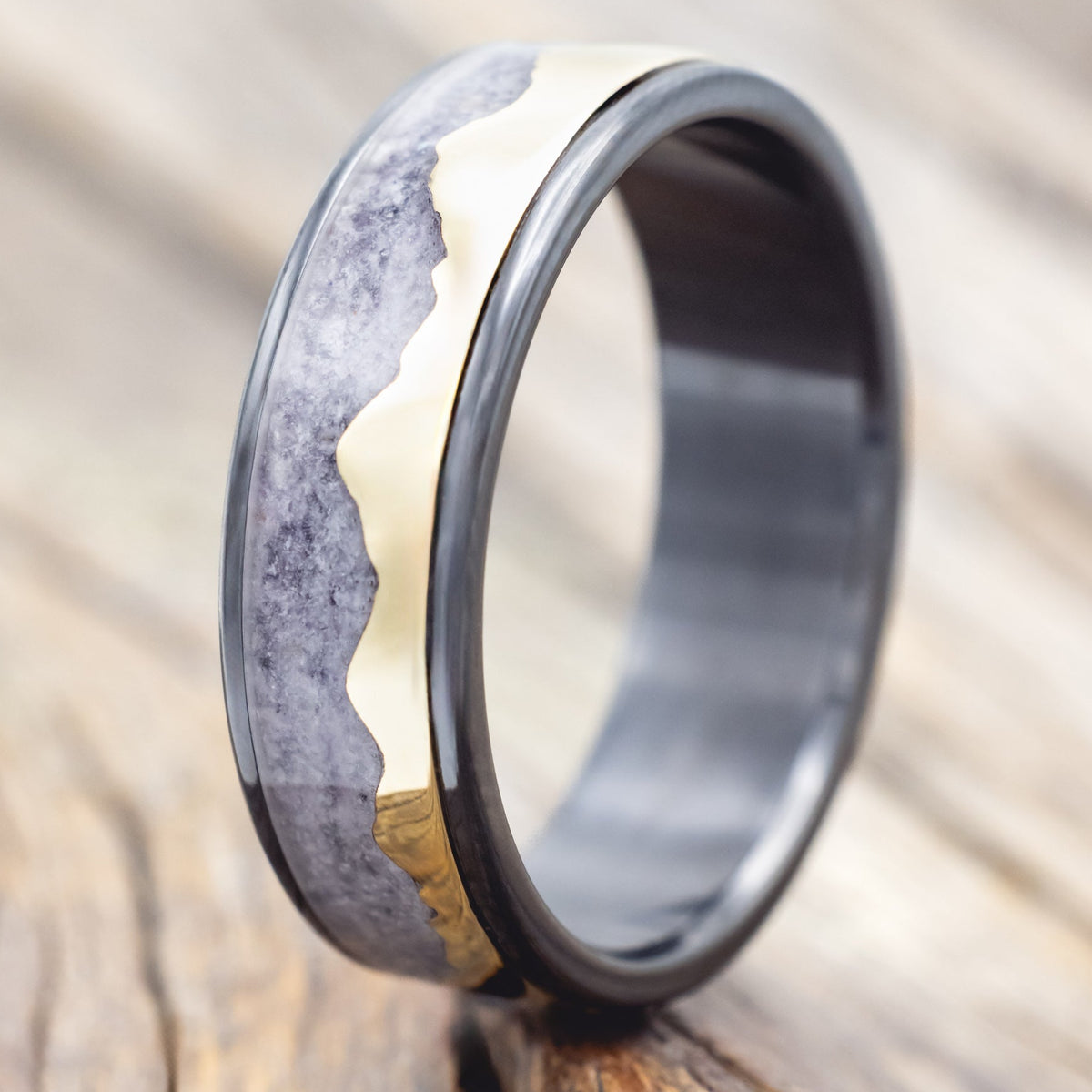 Black zirconium ring with 14K gold mountain design on a wooden surface