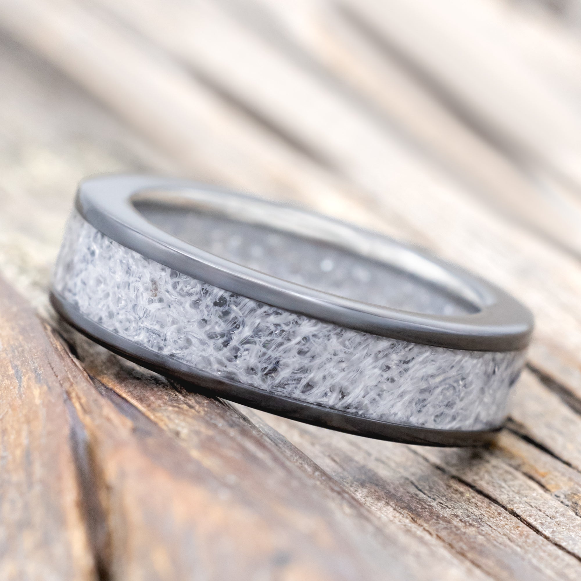 Black zirconium band with wedding dress inlay & diamond dust lining on a wooden surface