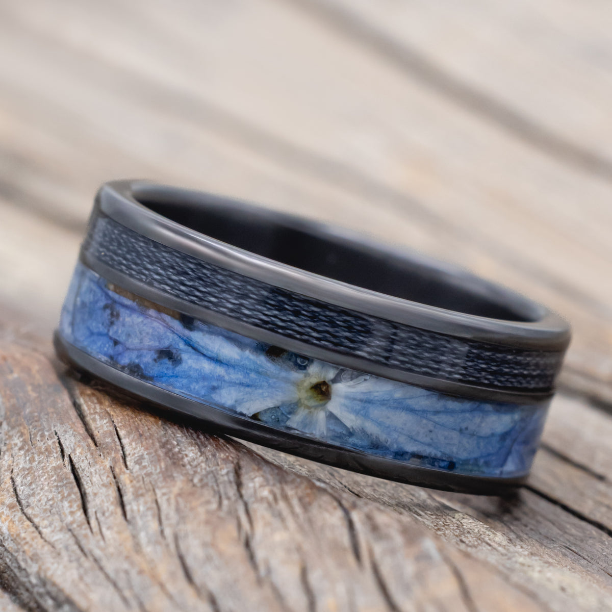 A black zirconium ring with fishing line and blue hydrangea inlays on a blurred wooden surface