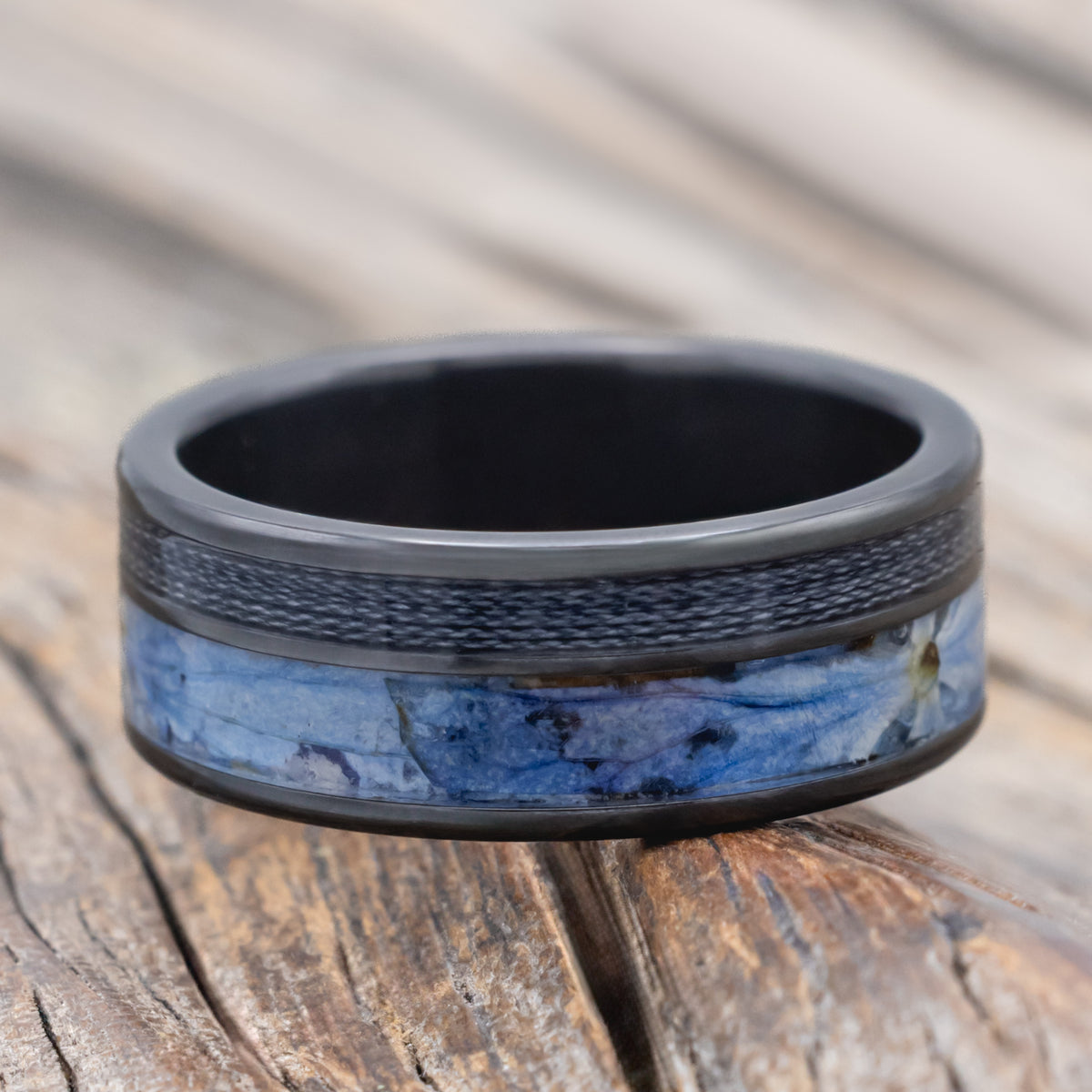 A black zirconium ring with fishing line and blue hydrangea inlays on a blurred wooden surface