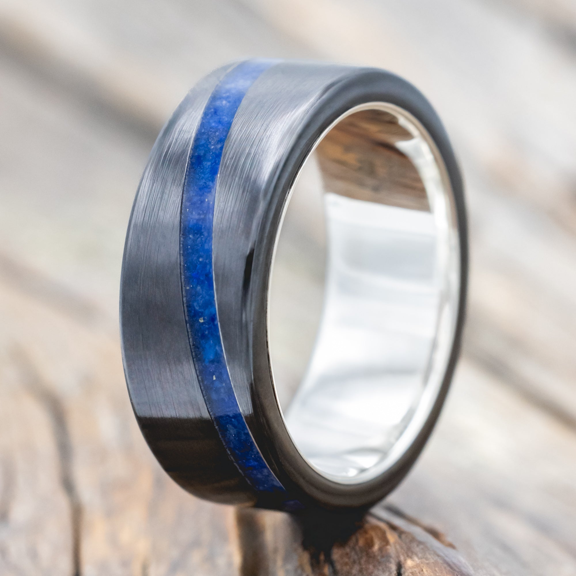 Black zirconium ring with lapis lazuli inlay and silver lining on a wooden surface