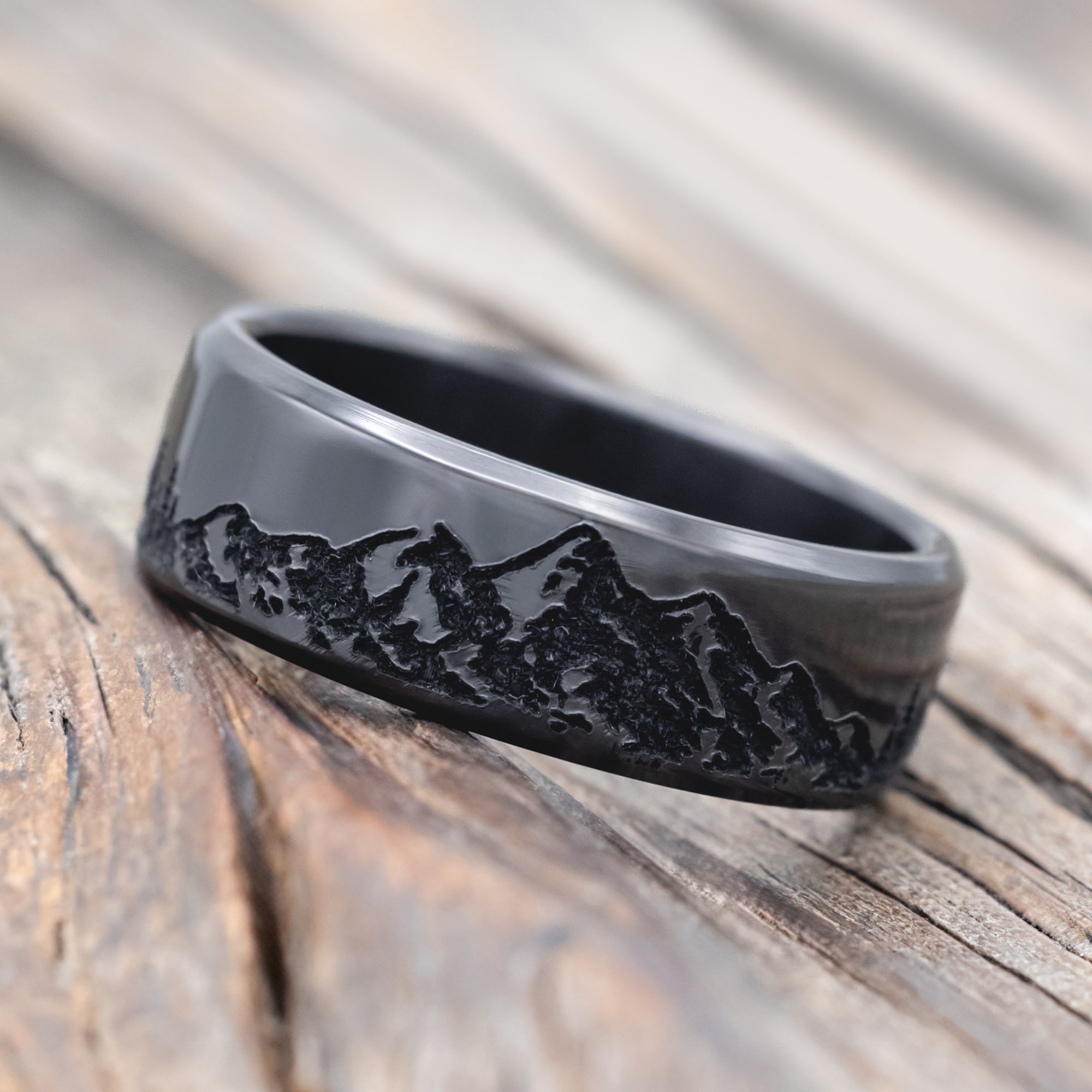 Black zirconium ring with mountain & tree engraving on a wooden surface