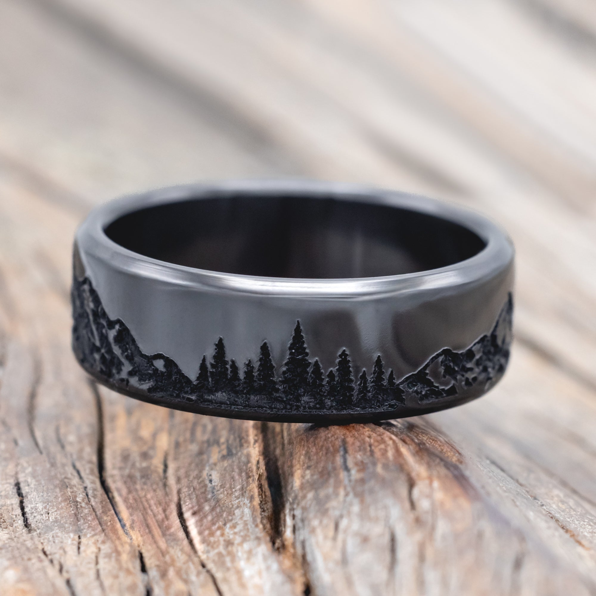 Black zirconium ring with mountain & tree engraving on a wooden surface