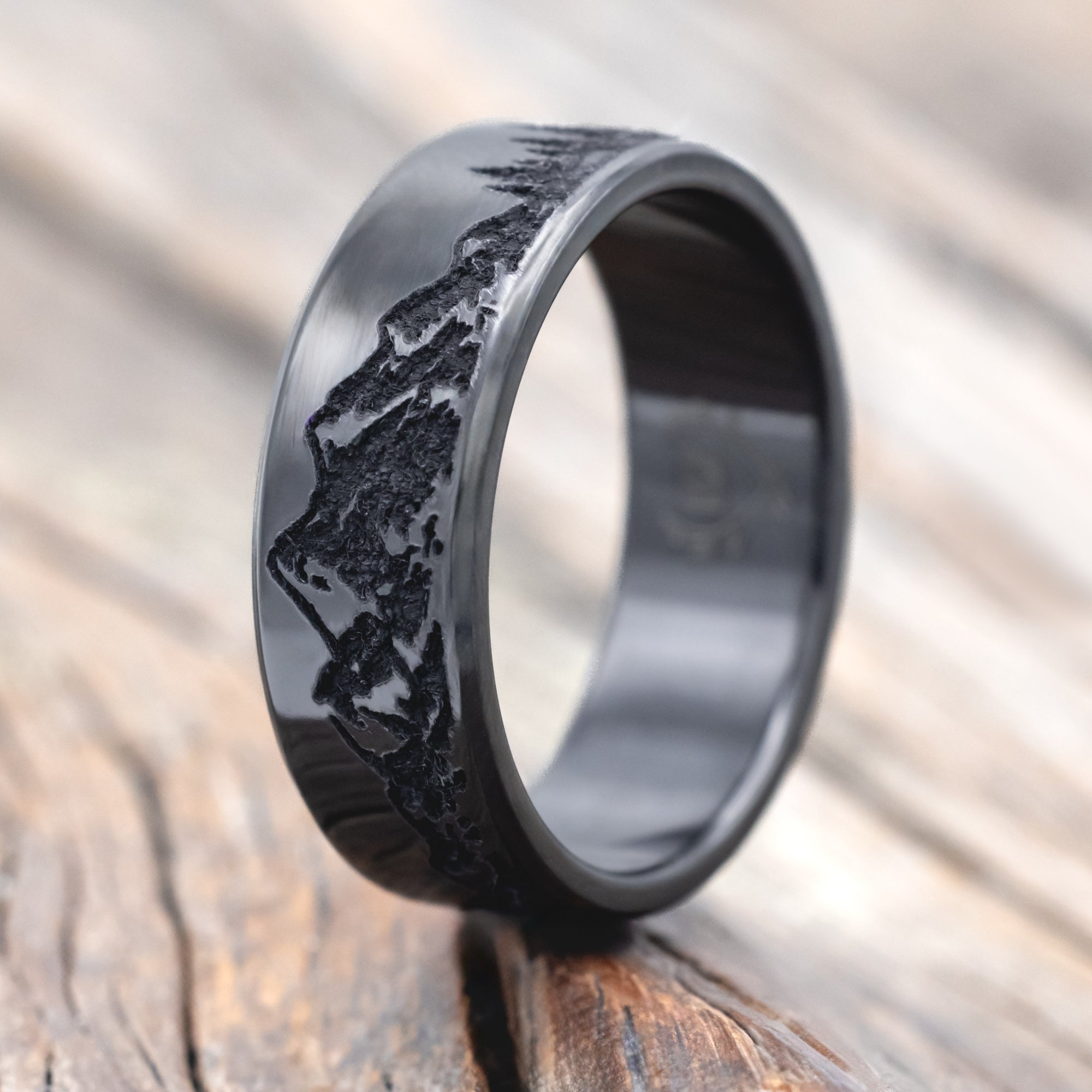 Black zirconium ring with mountain & tree engraving on a wooden surface