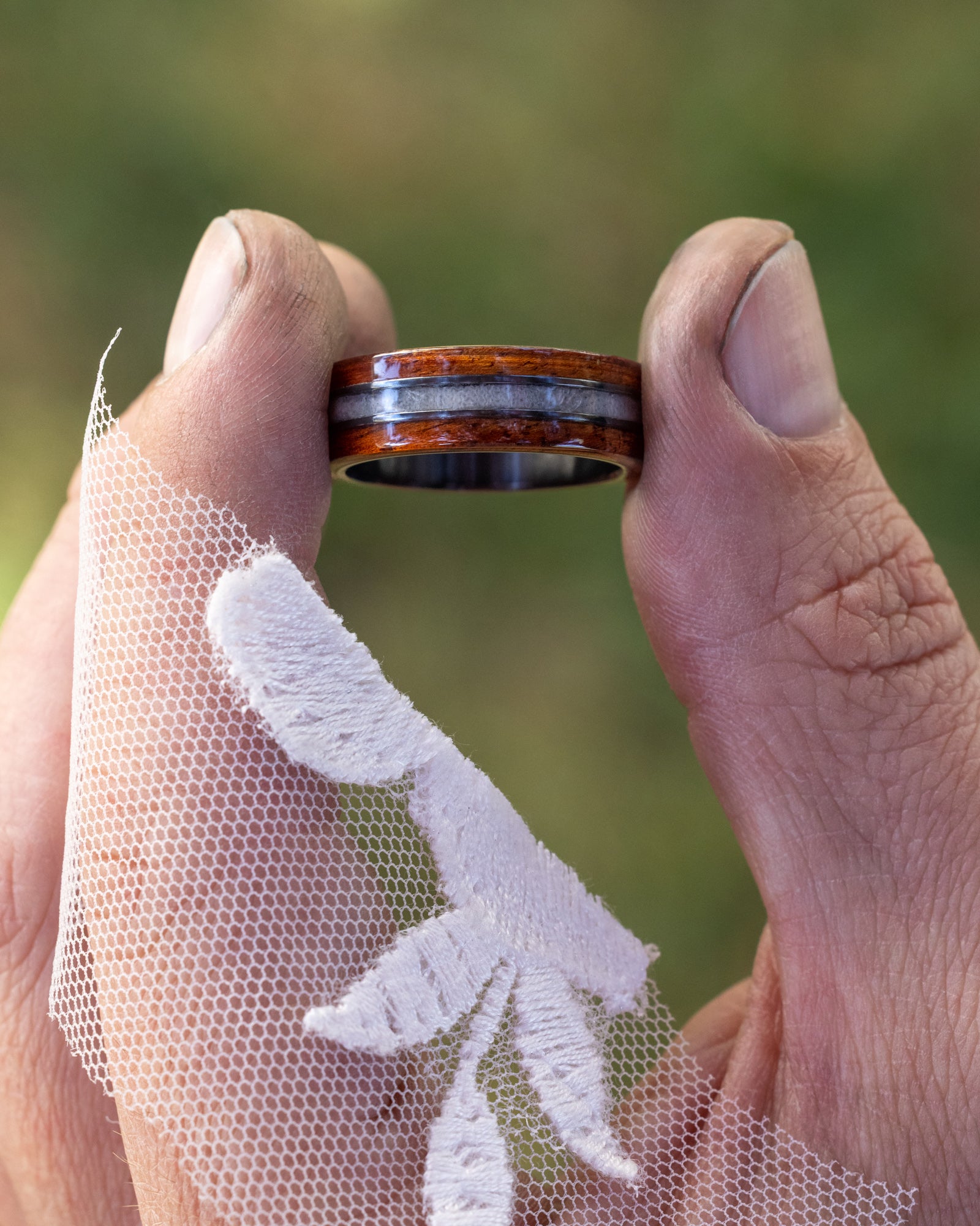 Hand holding a wooden ring with a blurred green background