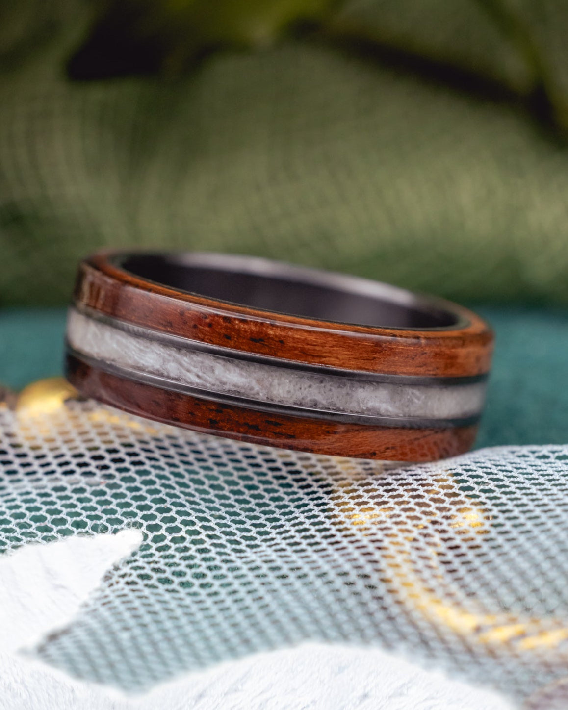 Black zirconium with koa wood and wedding dress inlay against a blurred green background