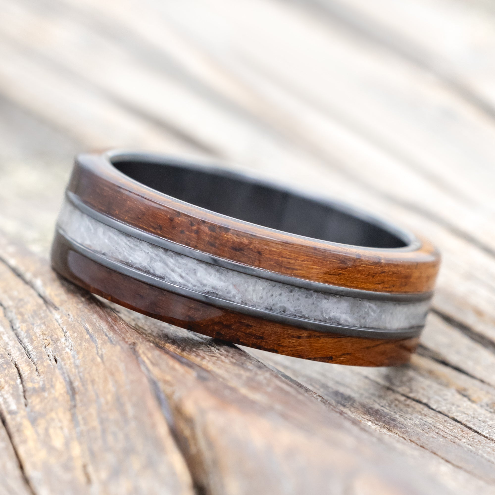 black zirconium wedding ring with koa wood and wedding dress inlay on wooden surface