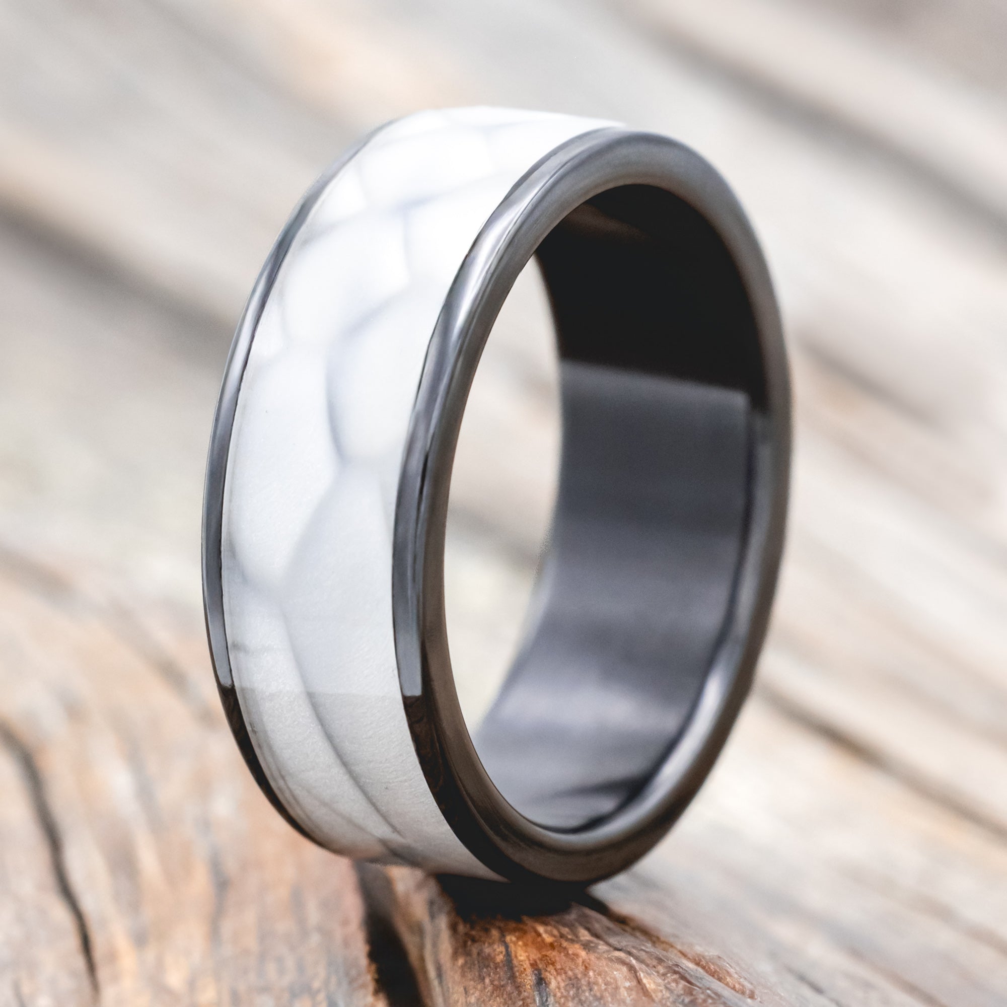 Black zirconium ring with faux white scale inlay on a wooden surface