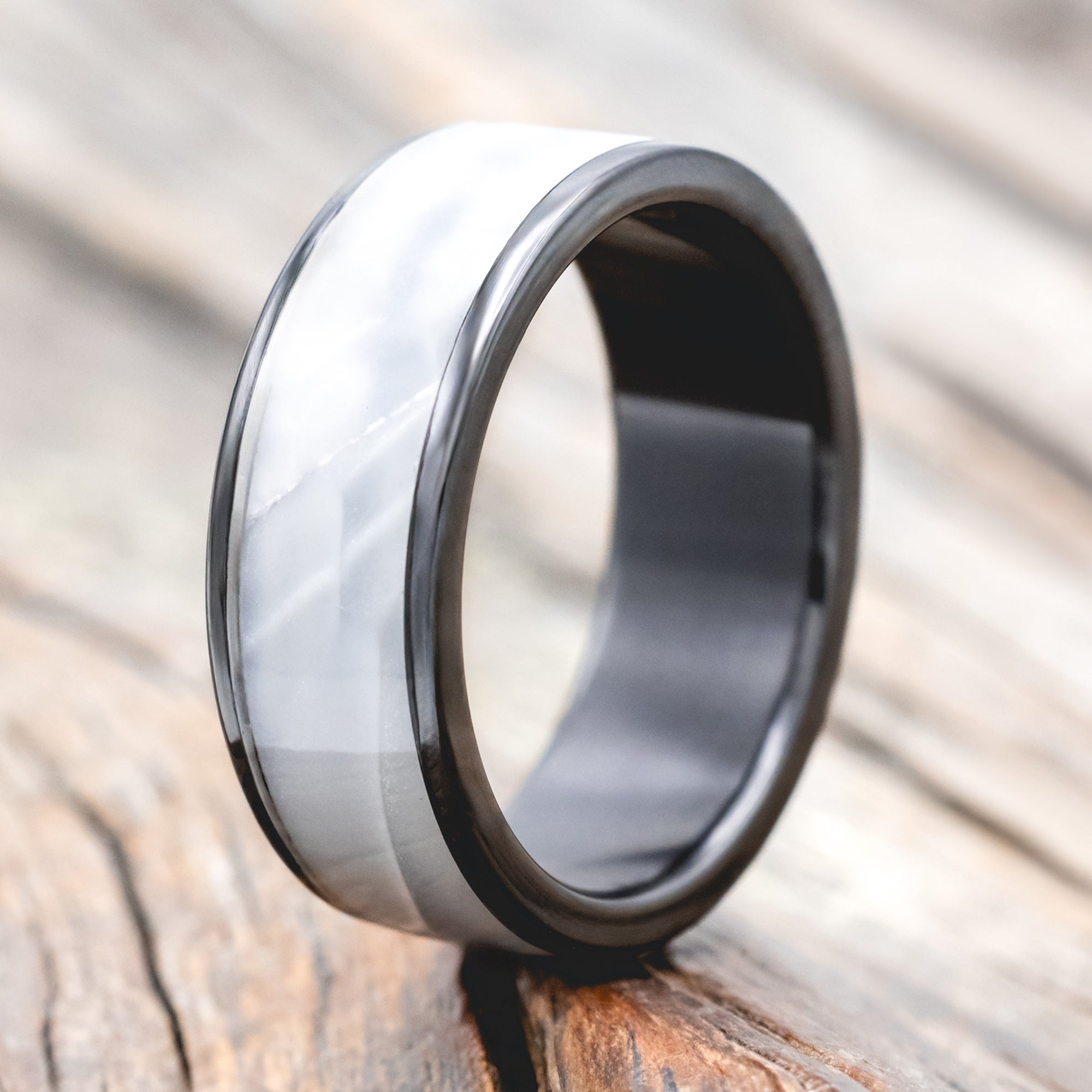 Black zirconium ring with faux white scale inlay on a wooden surface