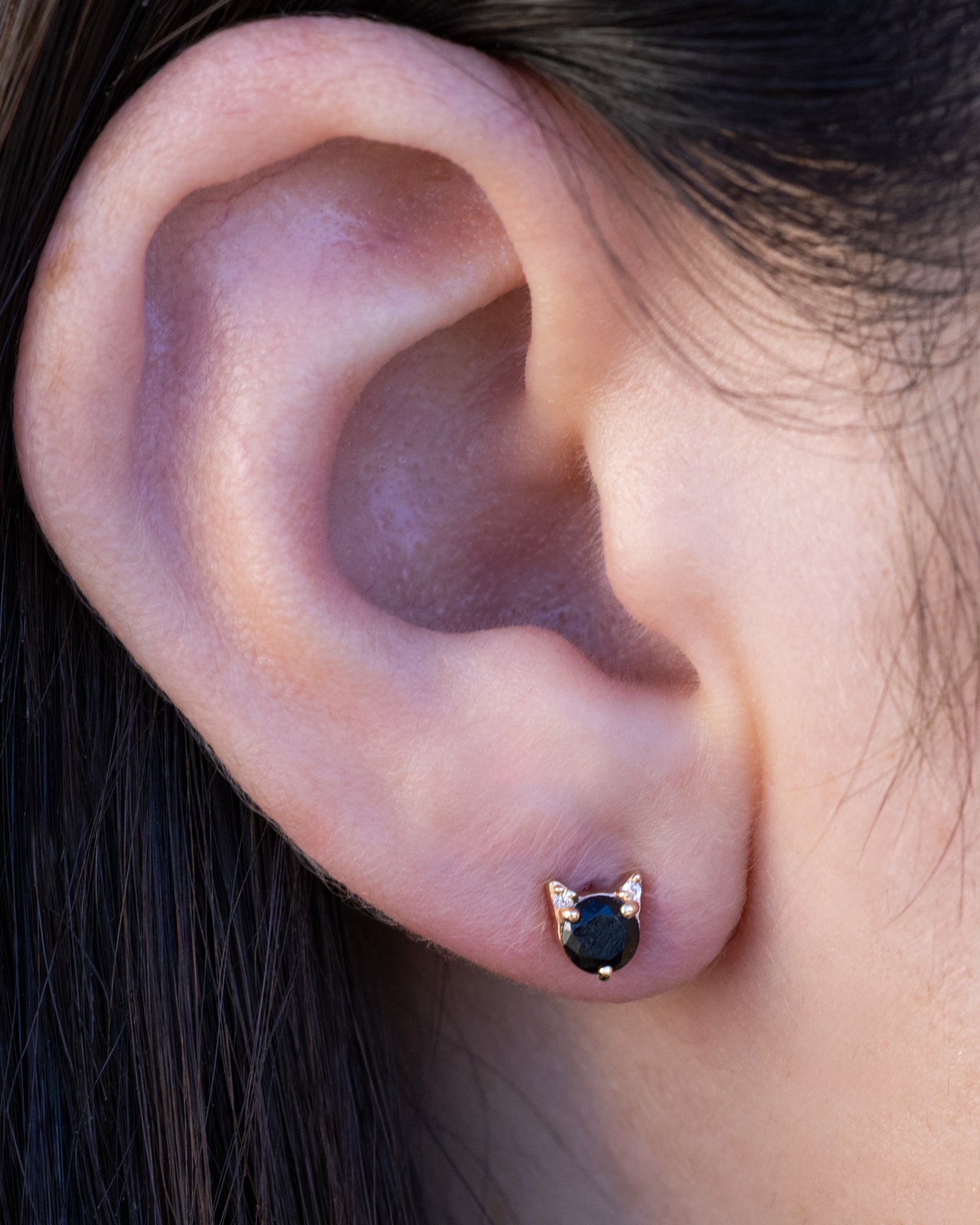 Onyx cat earring on the ear against dark hair