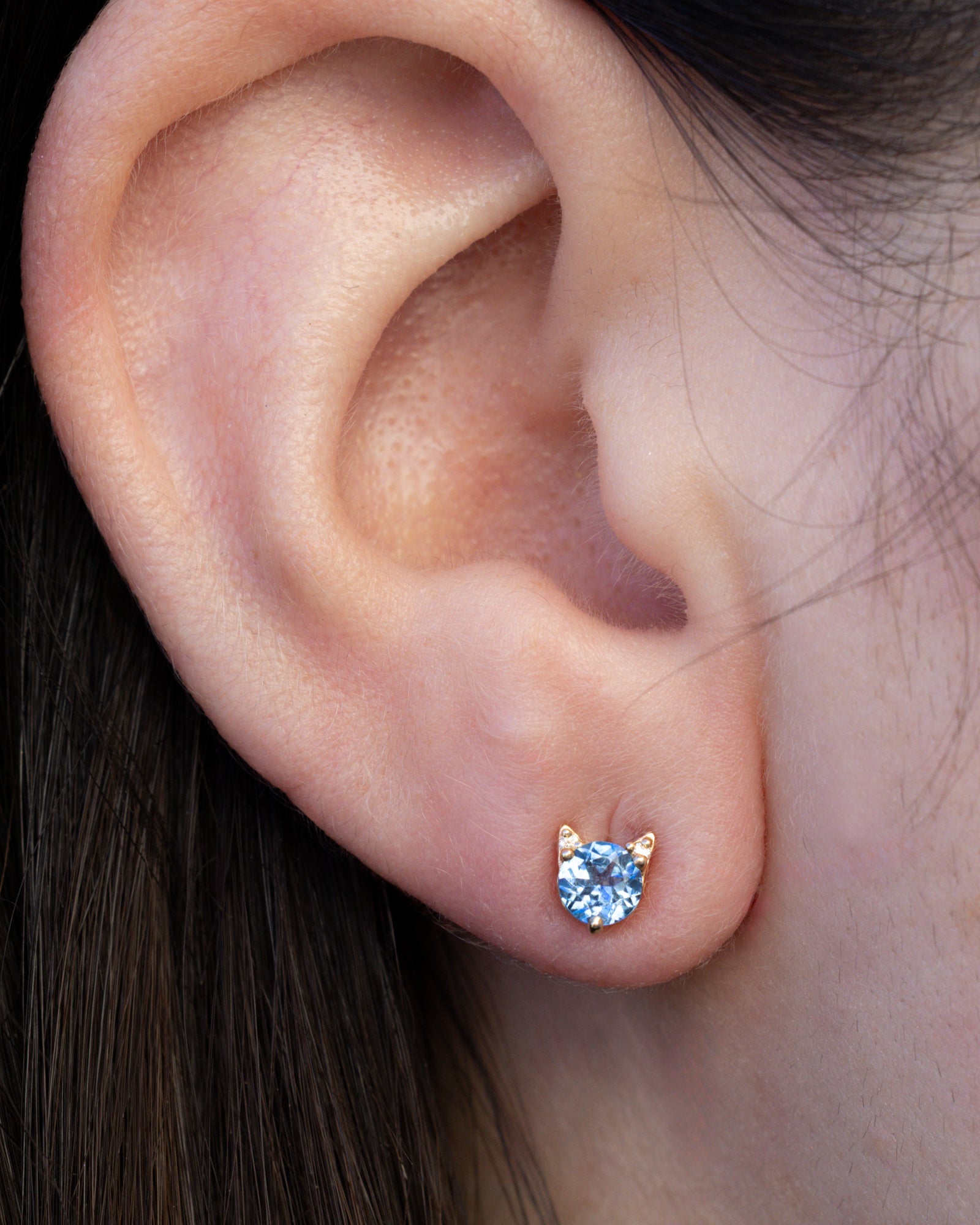 Montana sapphire cat earring on the ear against dark hair