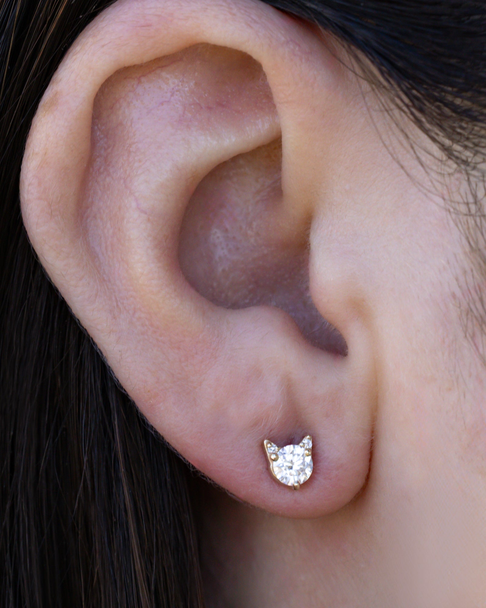 Moissanite cat earring on the ear against dark hair