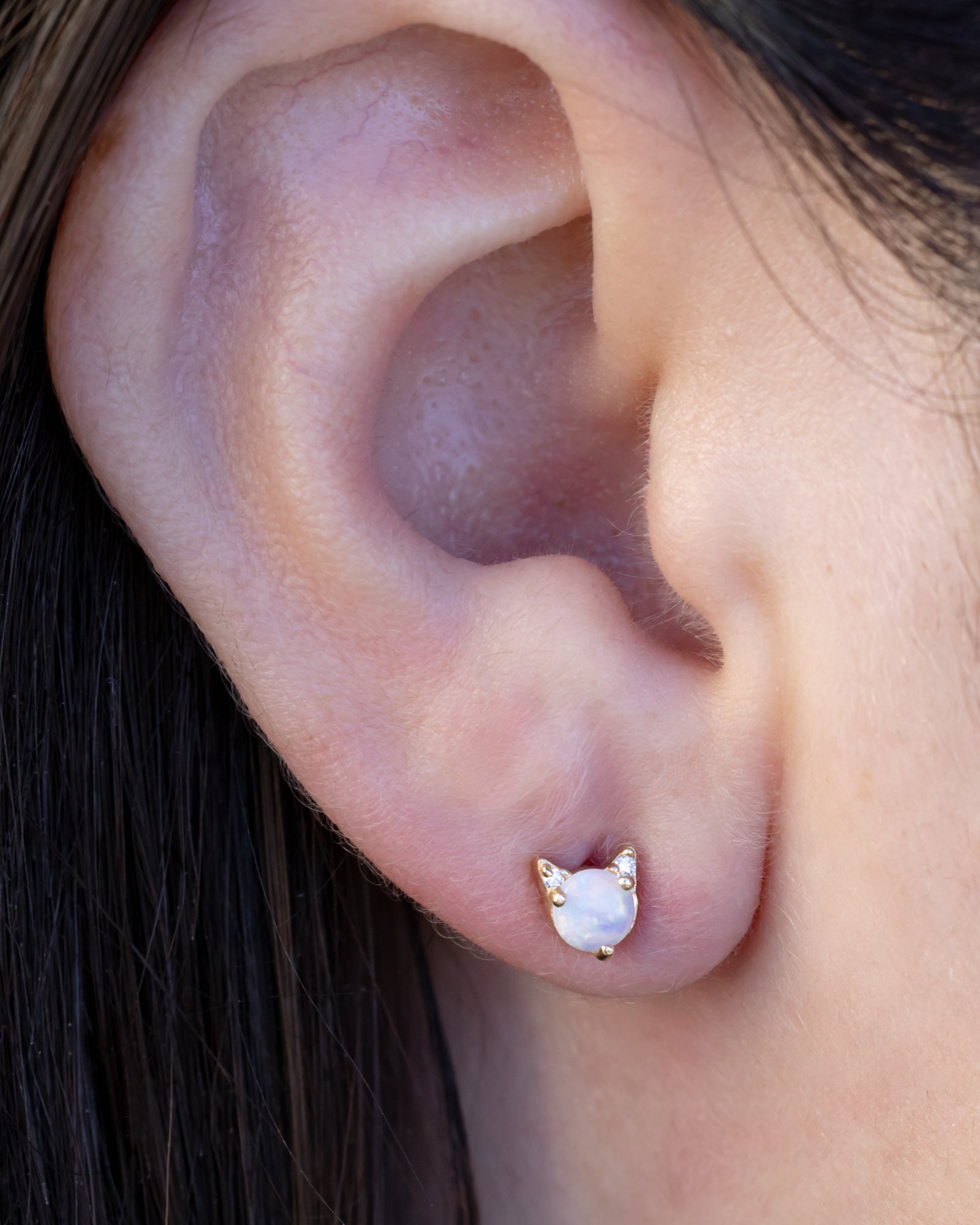 Opal cat earring on the ear against dark hair