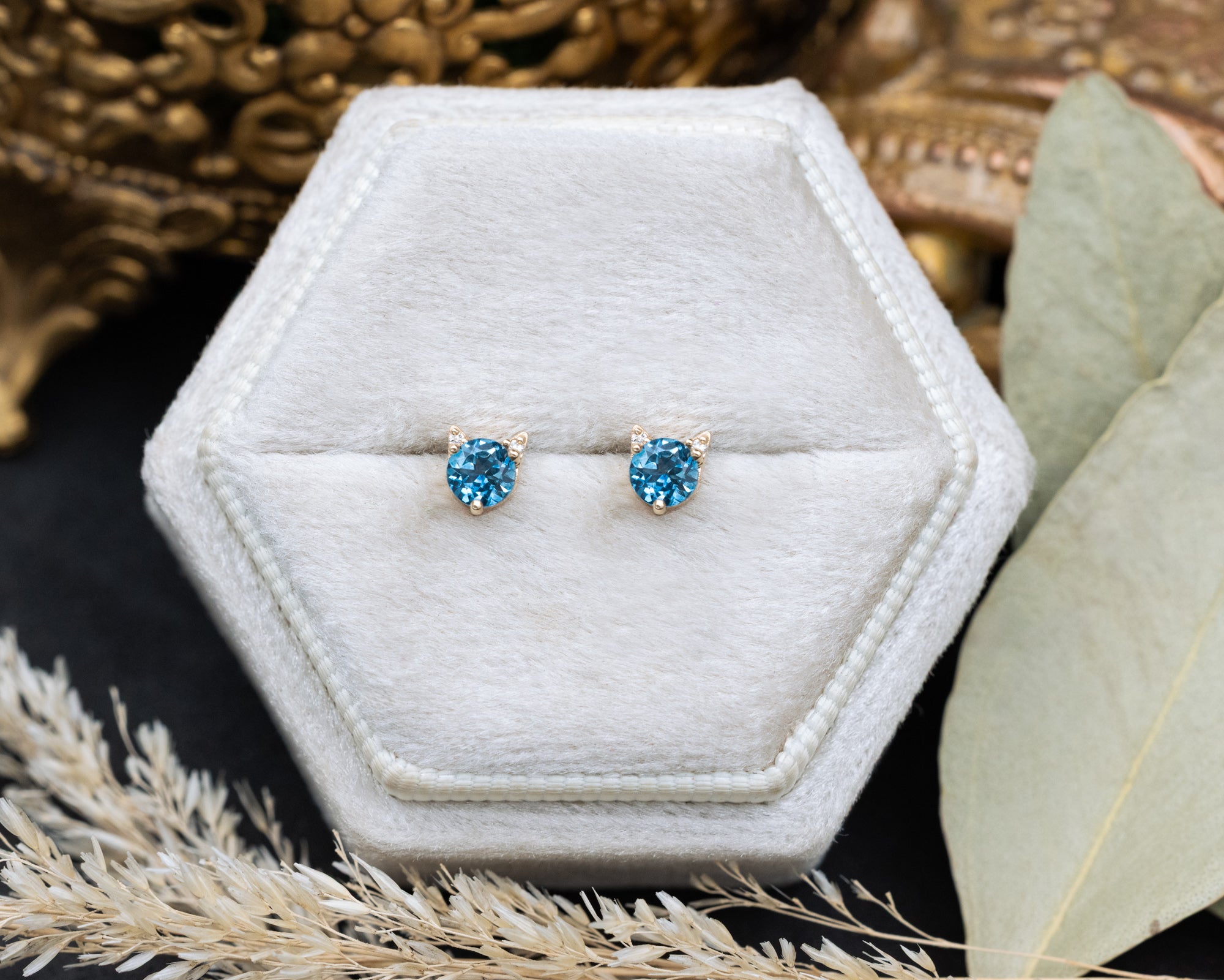 Pair of Montana sapphire cat-shaped stud earrings on a white cushion against a decorative background