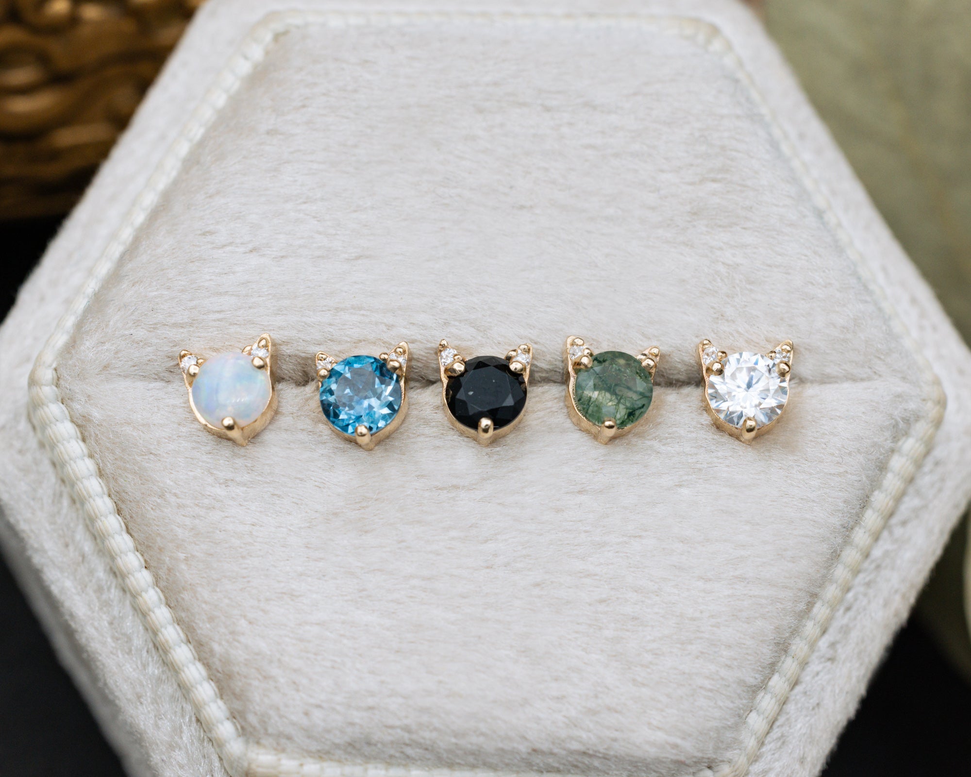 5 cat-shaped stud earrings on a white cushion against a decorative background