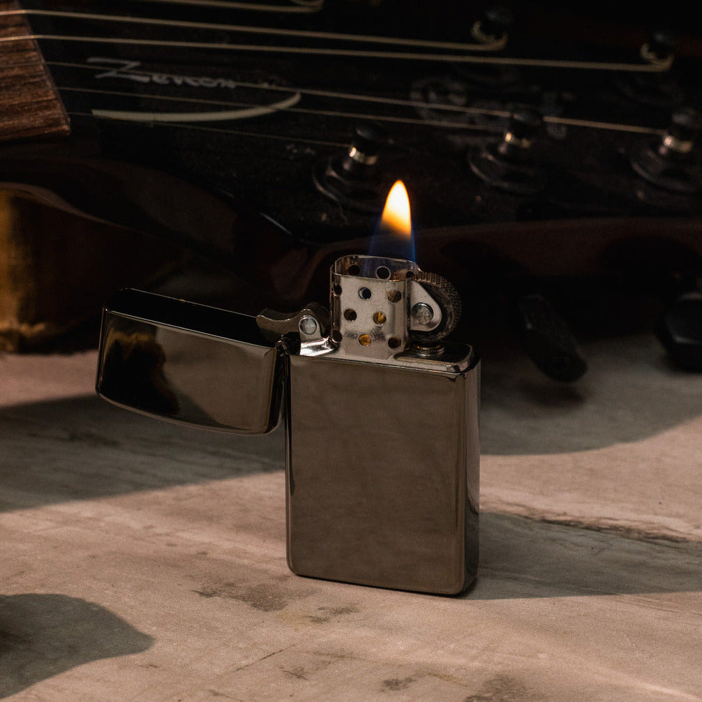 Zippo lighter with flame on a wooden surface with a blurred natural background