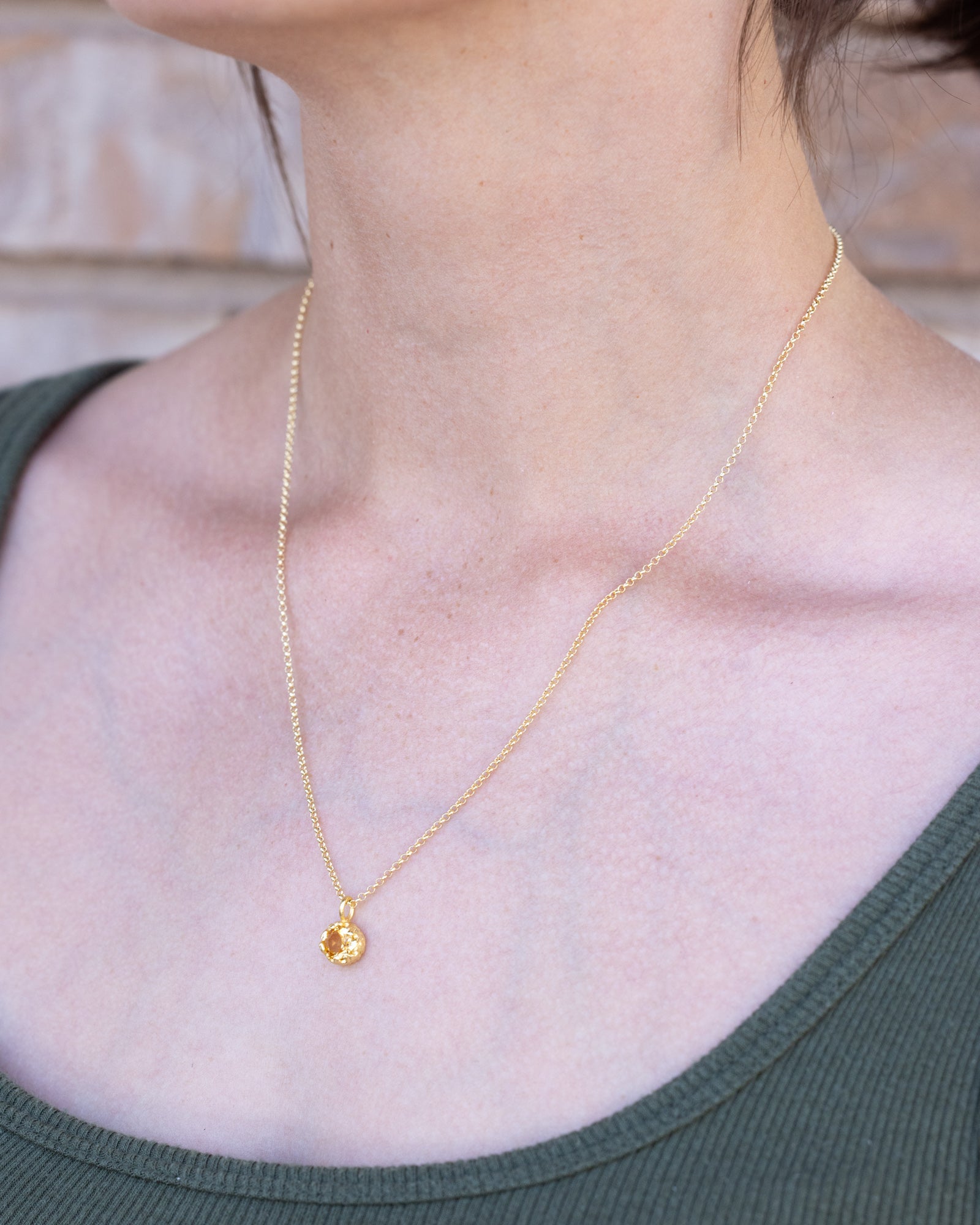 Gold necklace with a small citrine pendant worn by a person in a green top.