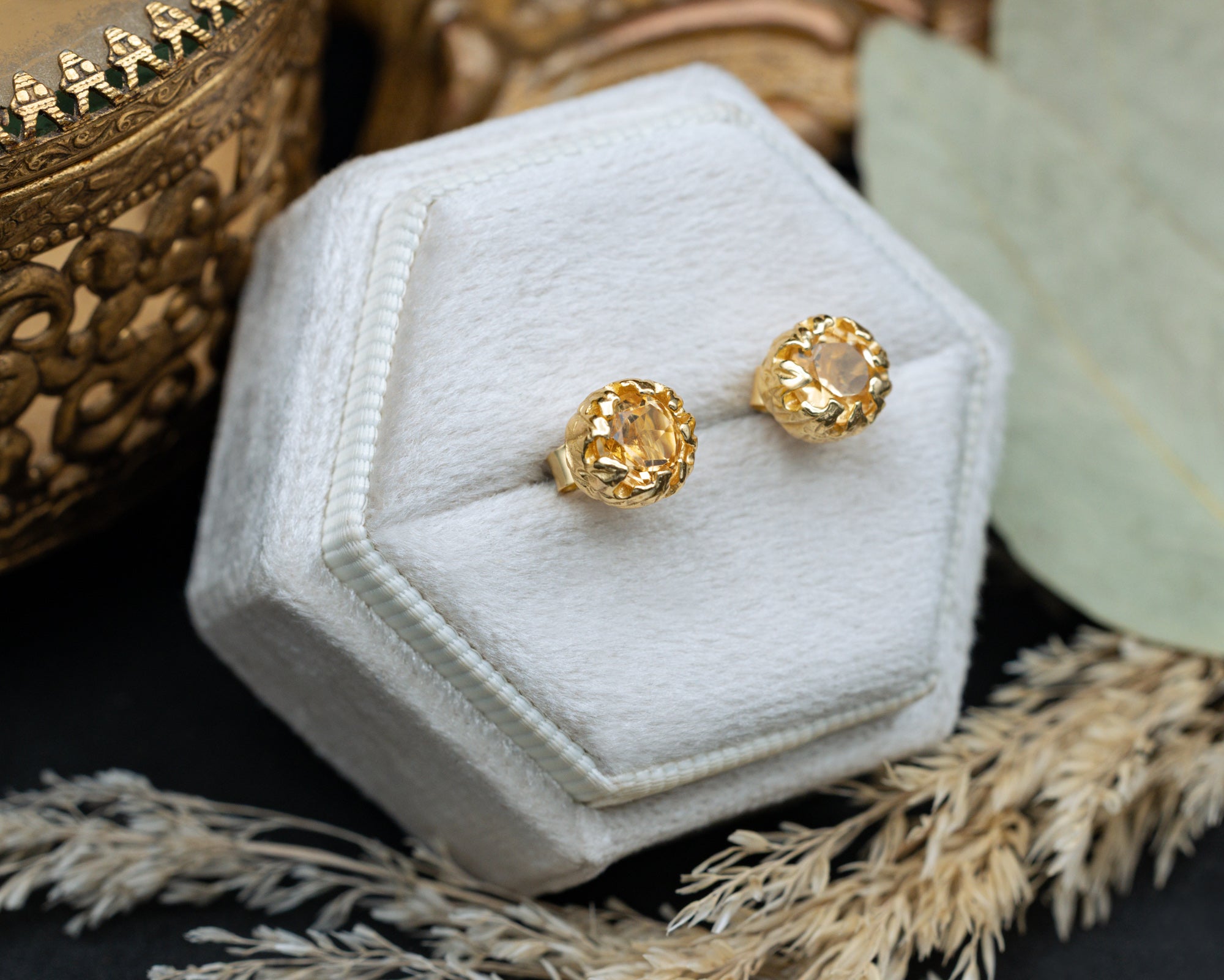 Gold citrine earrings in a white hexagonal jewelry box with decorative elements.
