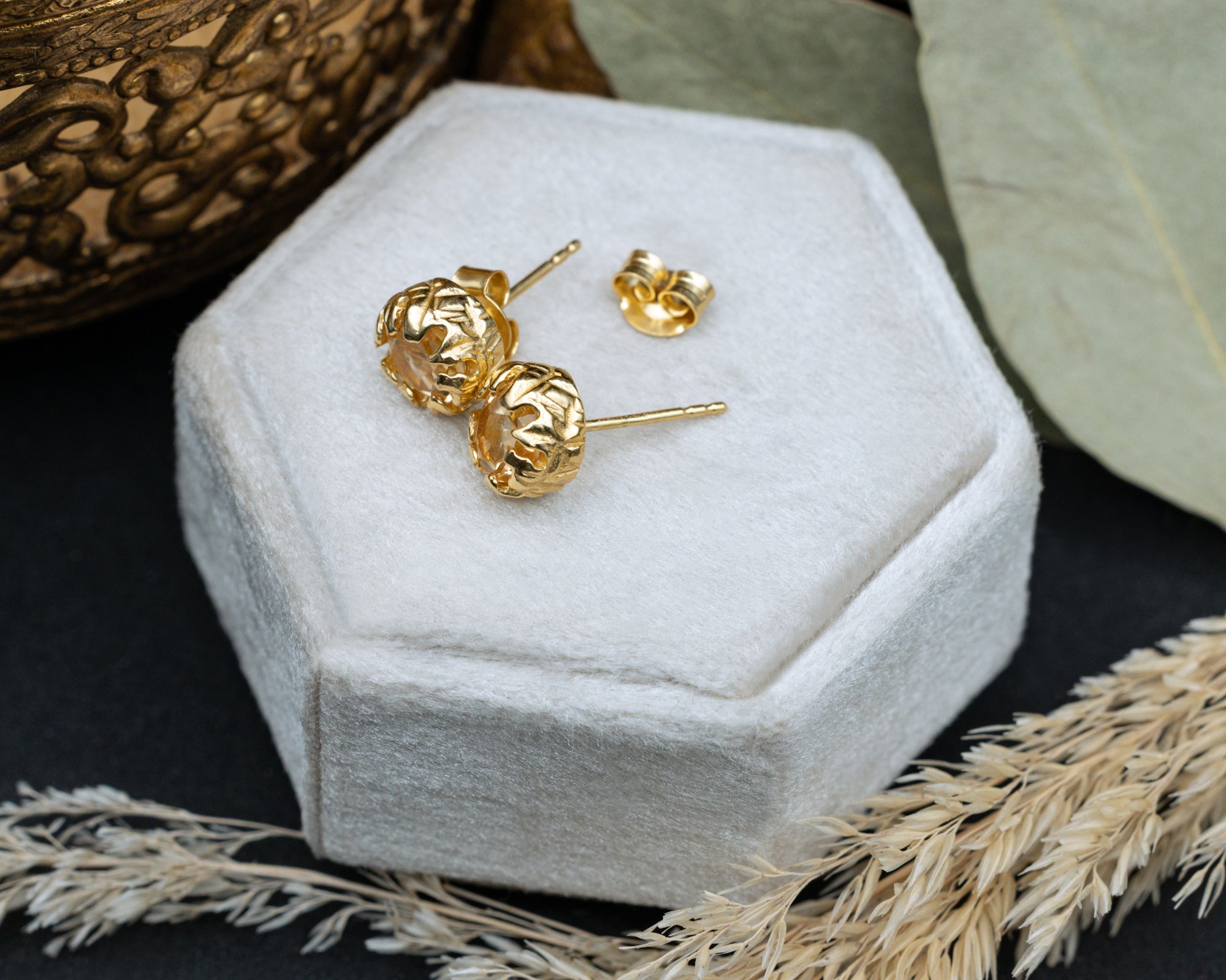 Gold citrine earrings on a white hexagonal jewelry box with decorative elements.
