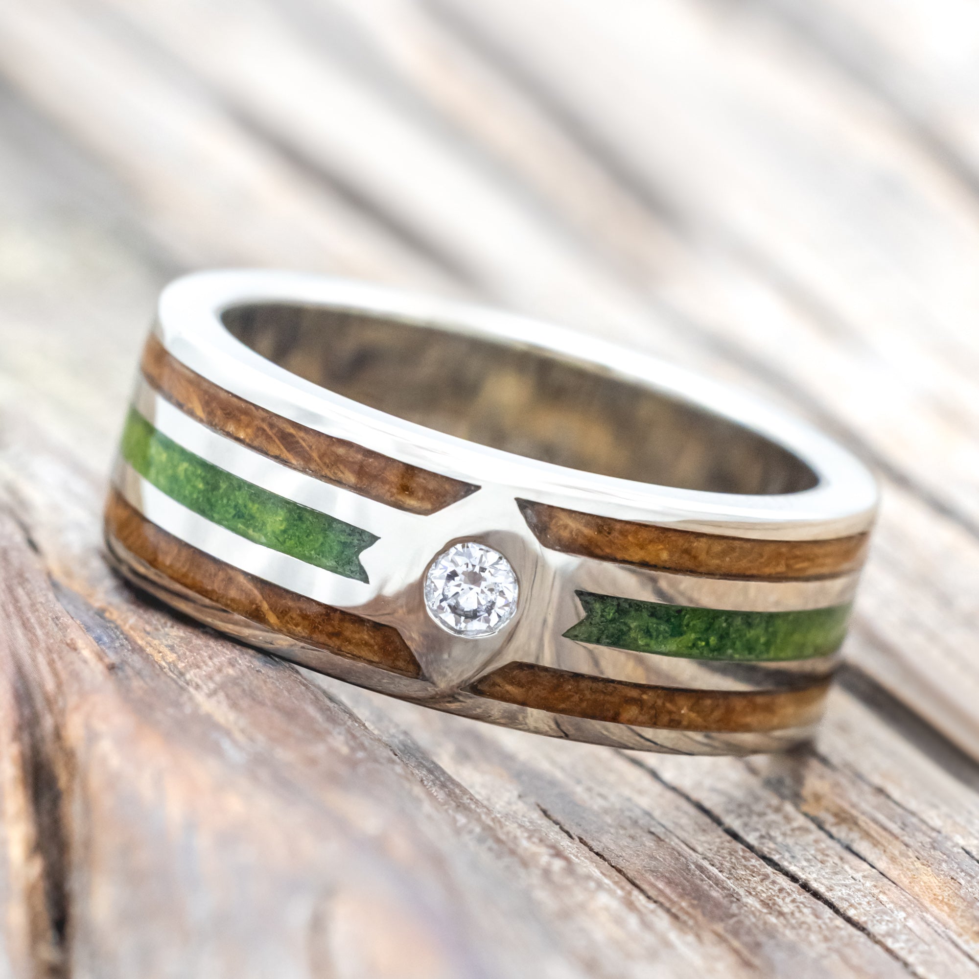 White gold ring with whiskey barrel oak and moss inlay and diamond accent on a wooden surface