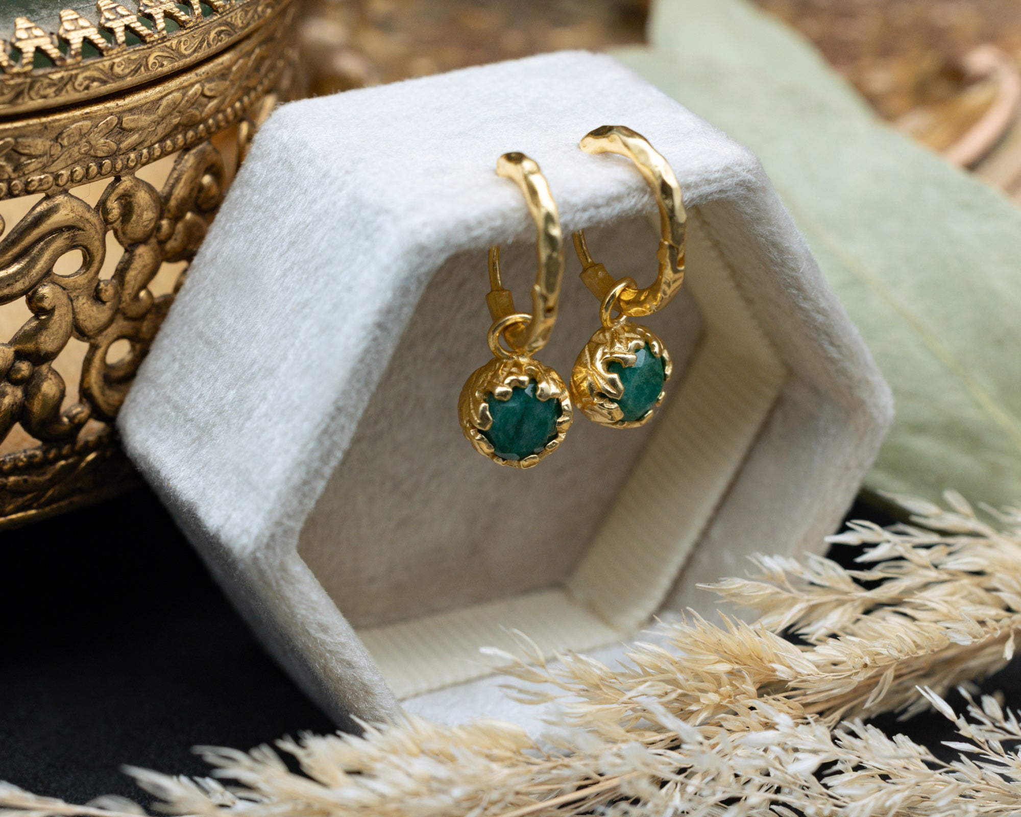 Gold earrings with green emeralds in a jewelry box on a textured surface