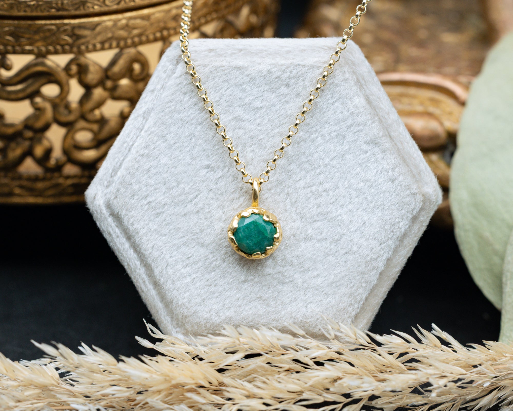 Gold necklace with a emerald pendant on a white hexagonal stand.