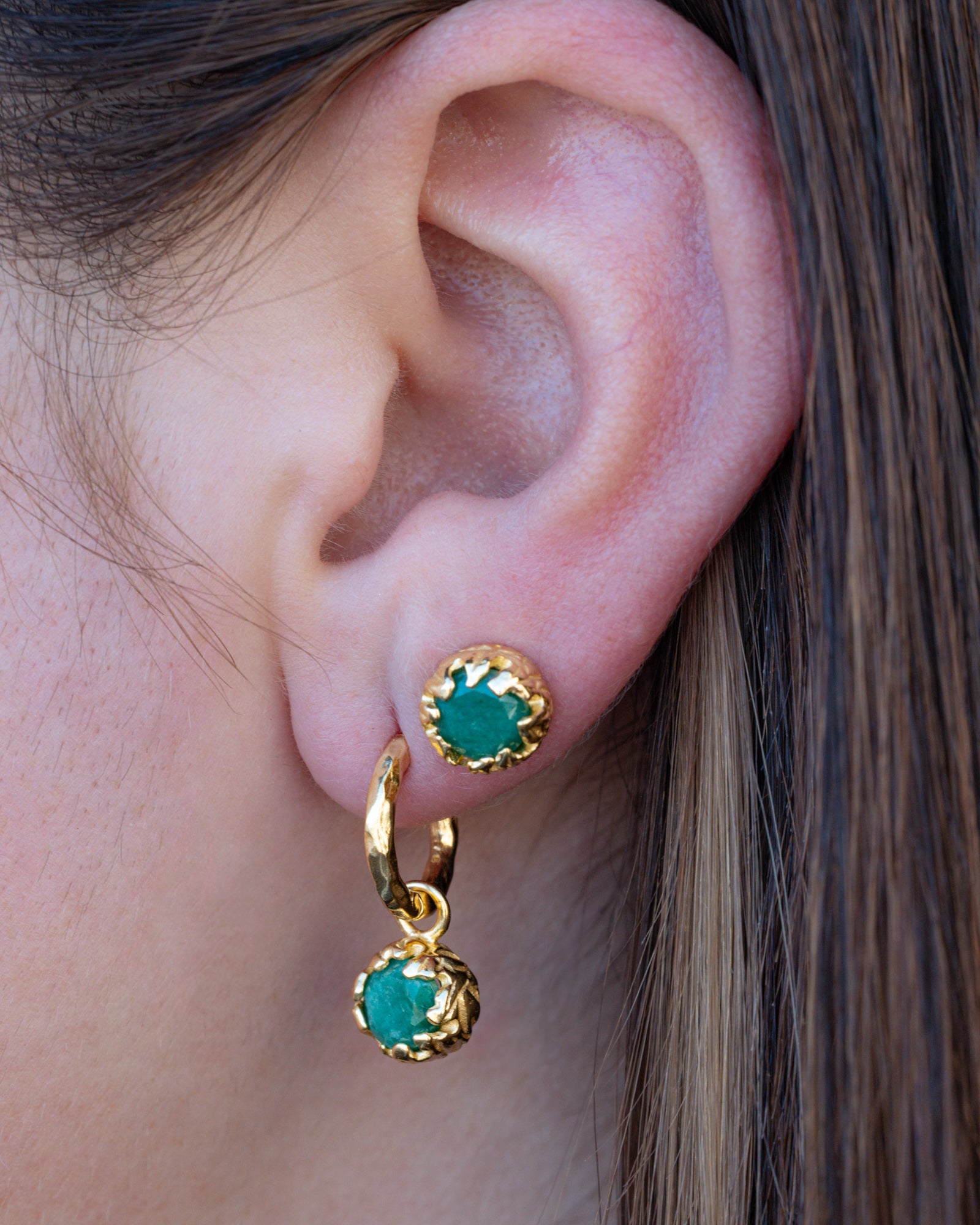 Gold earrings with green emerald worn by a person