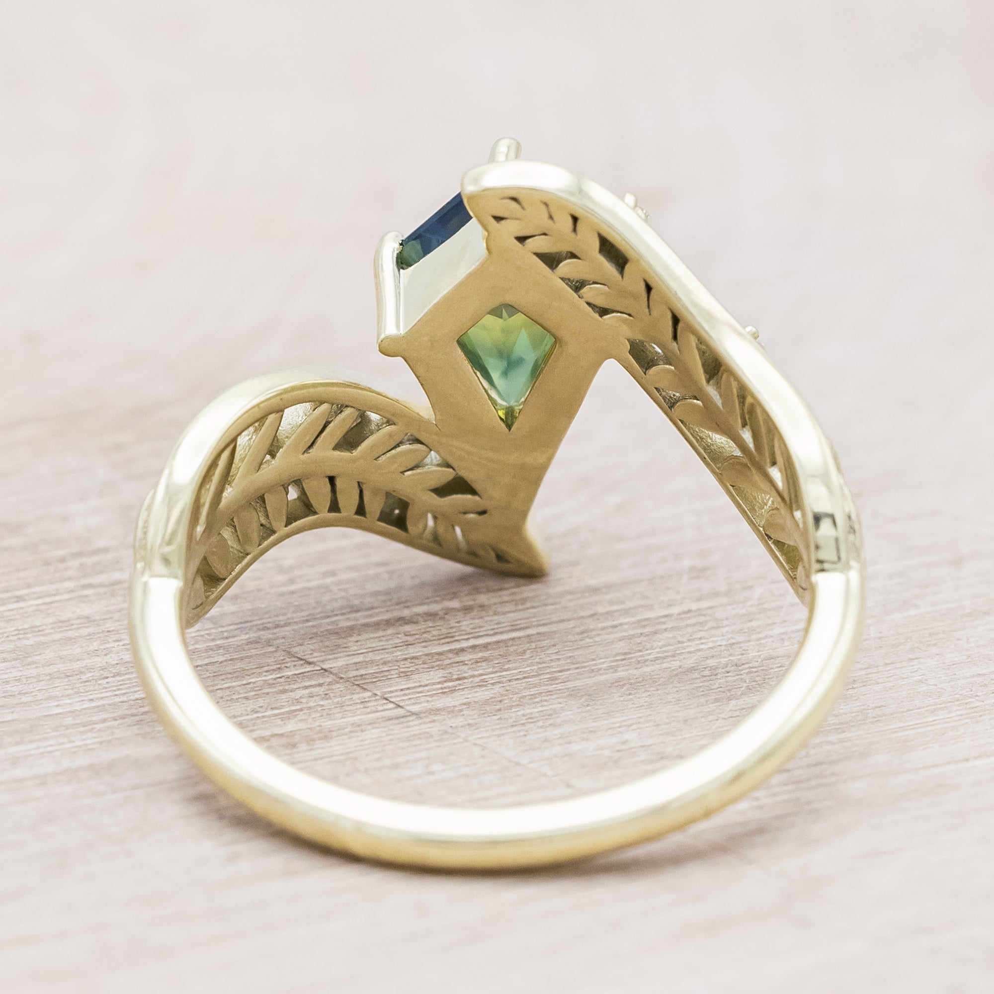 Green gold ring with a green sapphire on a light wooden surface
