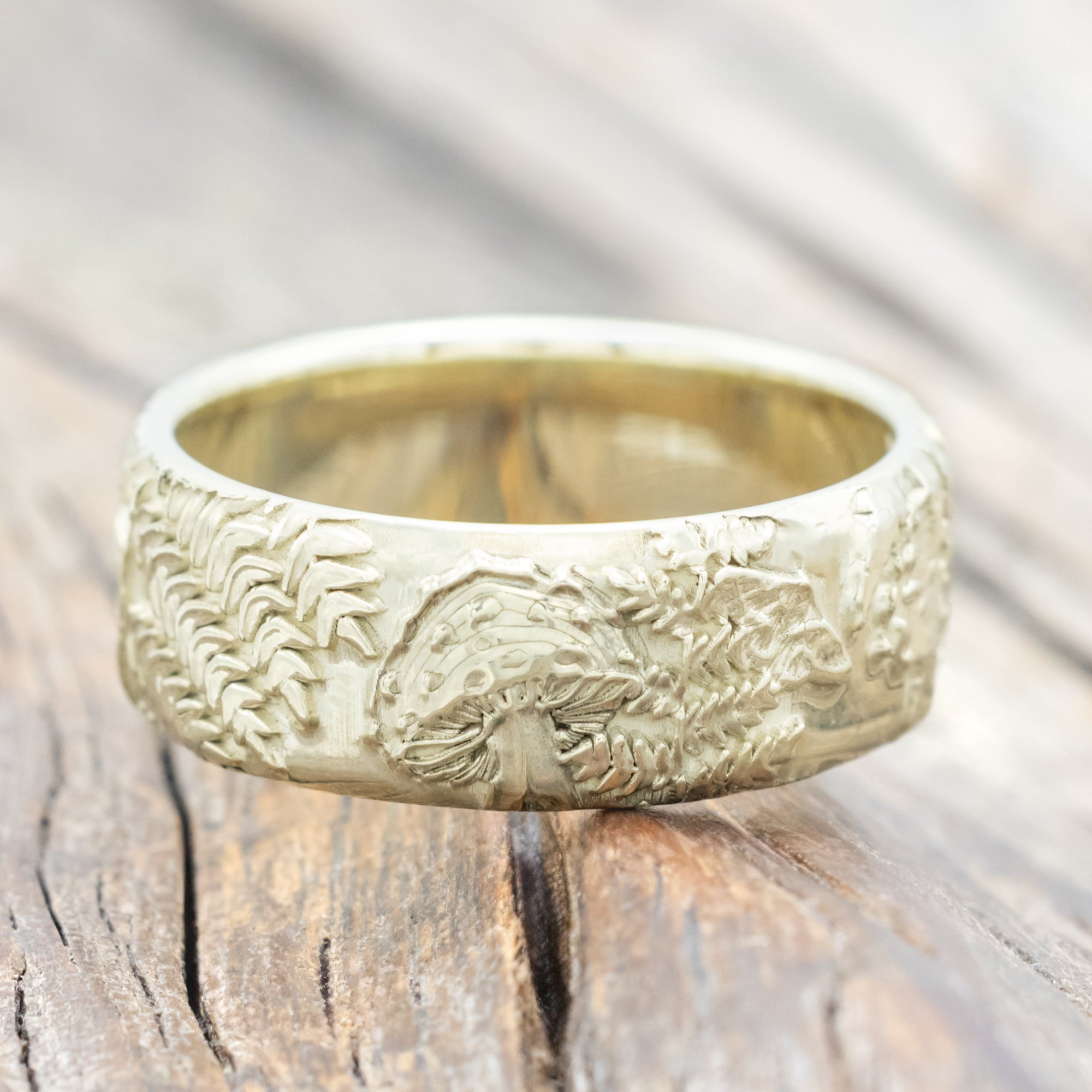 Green gold ring with intricate engravings on a wooden surface