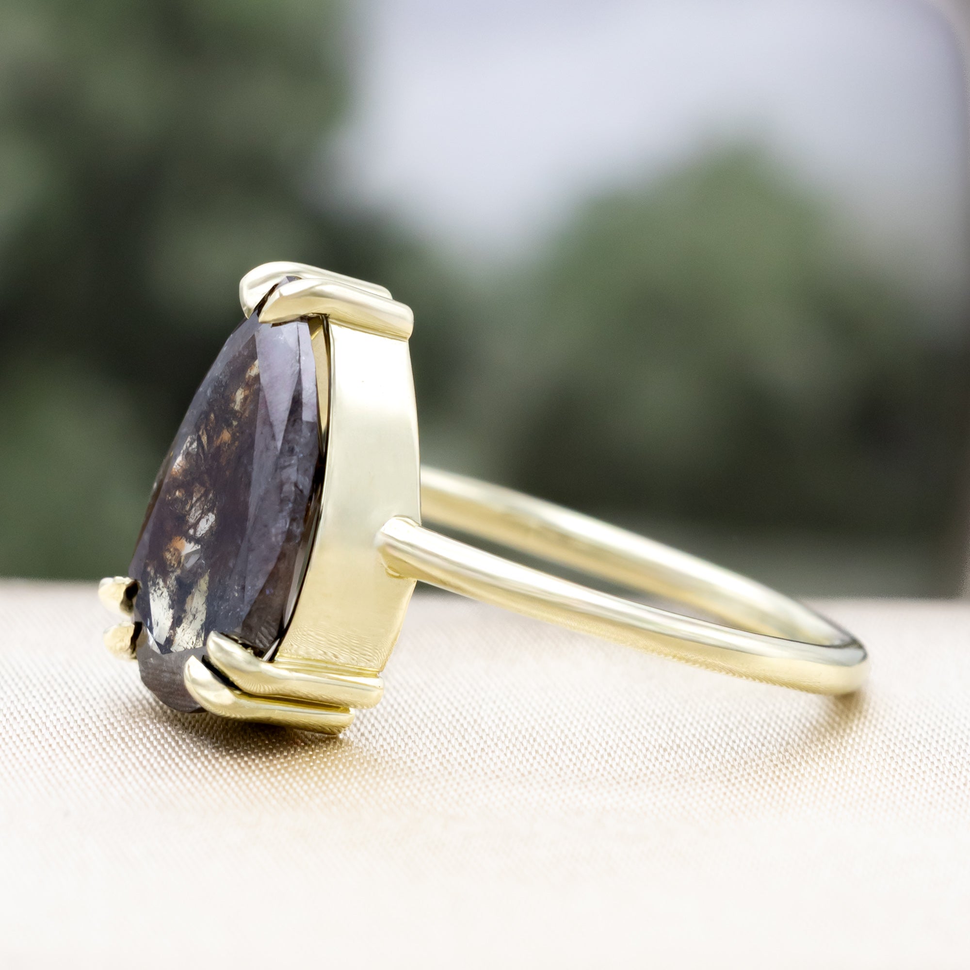 Solitaire green gold ring with a pear salt & pepper diamond centerstone against a blurred background