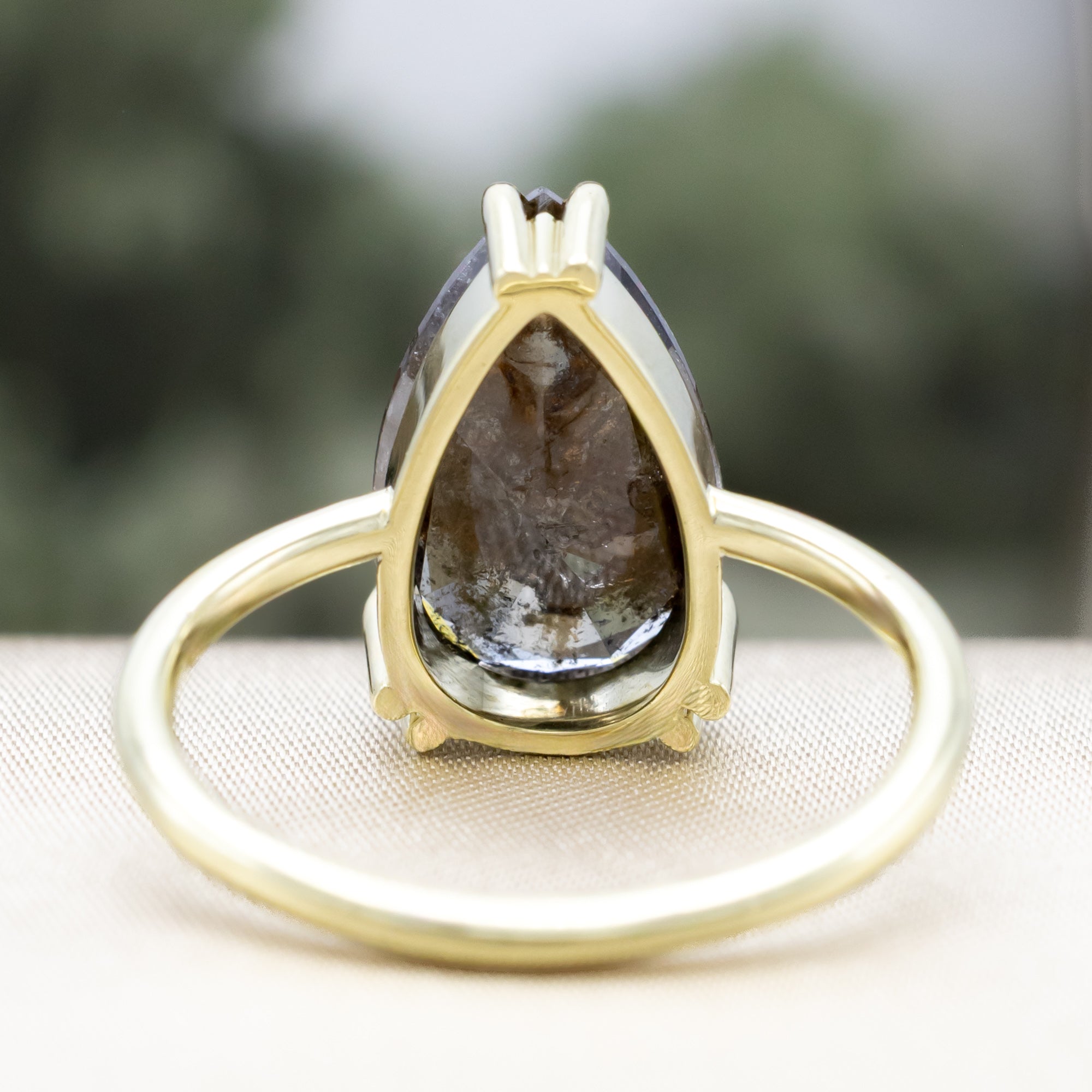 Solitaire green gold ring with a pear salt & pepper diamond centerstone against a blurred background