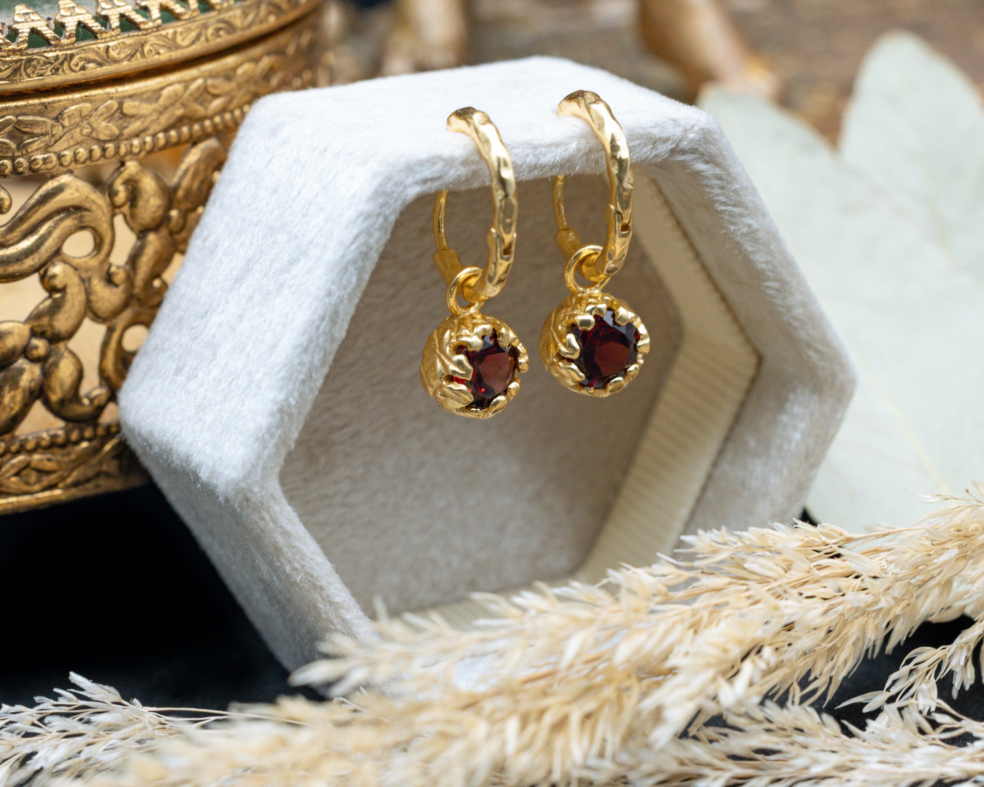 Gold earrings with red garnets on a white stand with a decorative background
