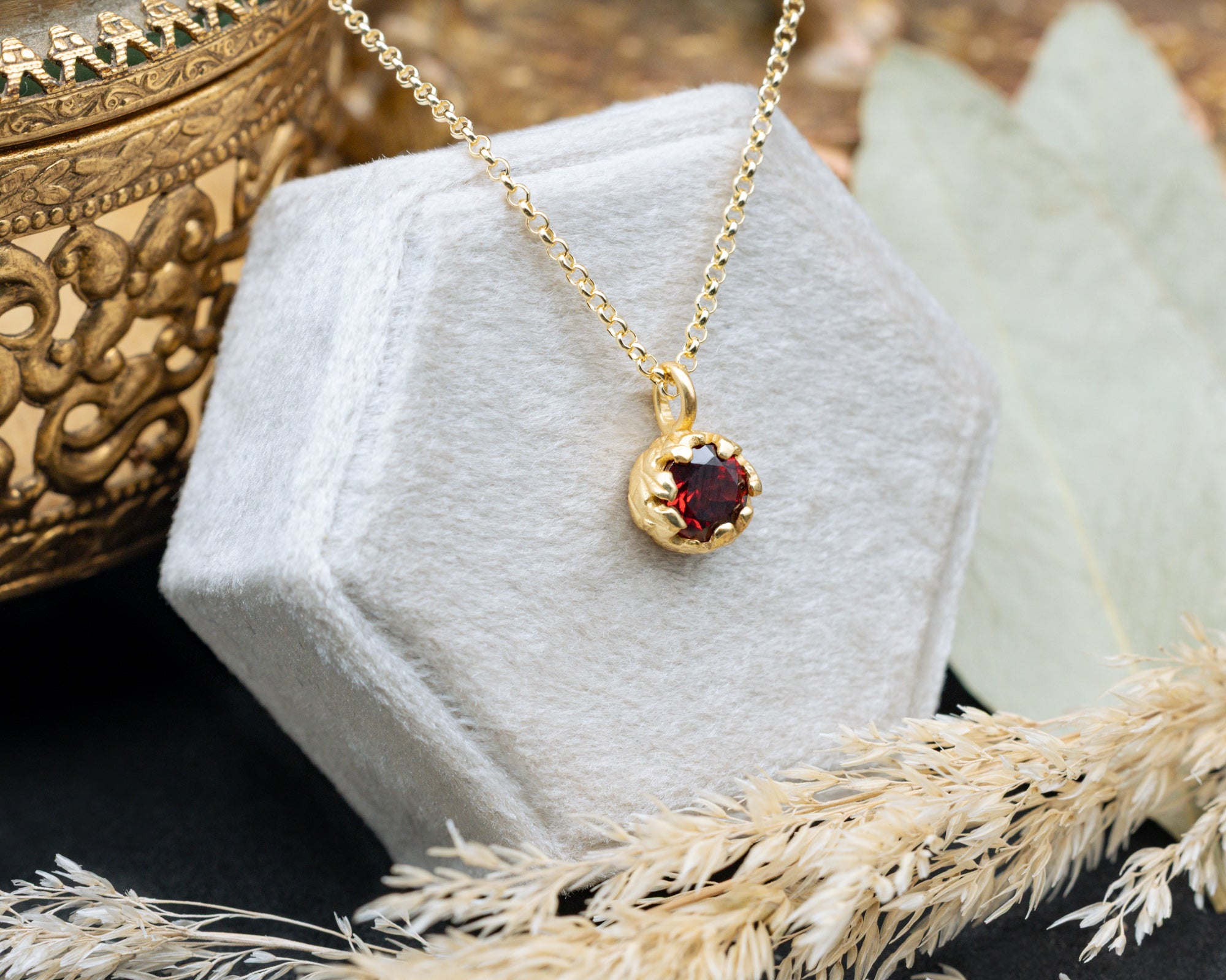Gold necklace with a red garnet on a white stand with a textured background