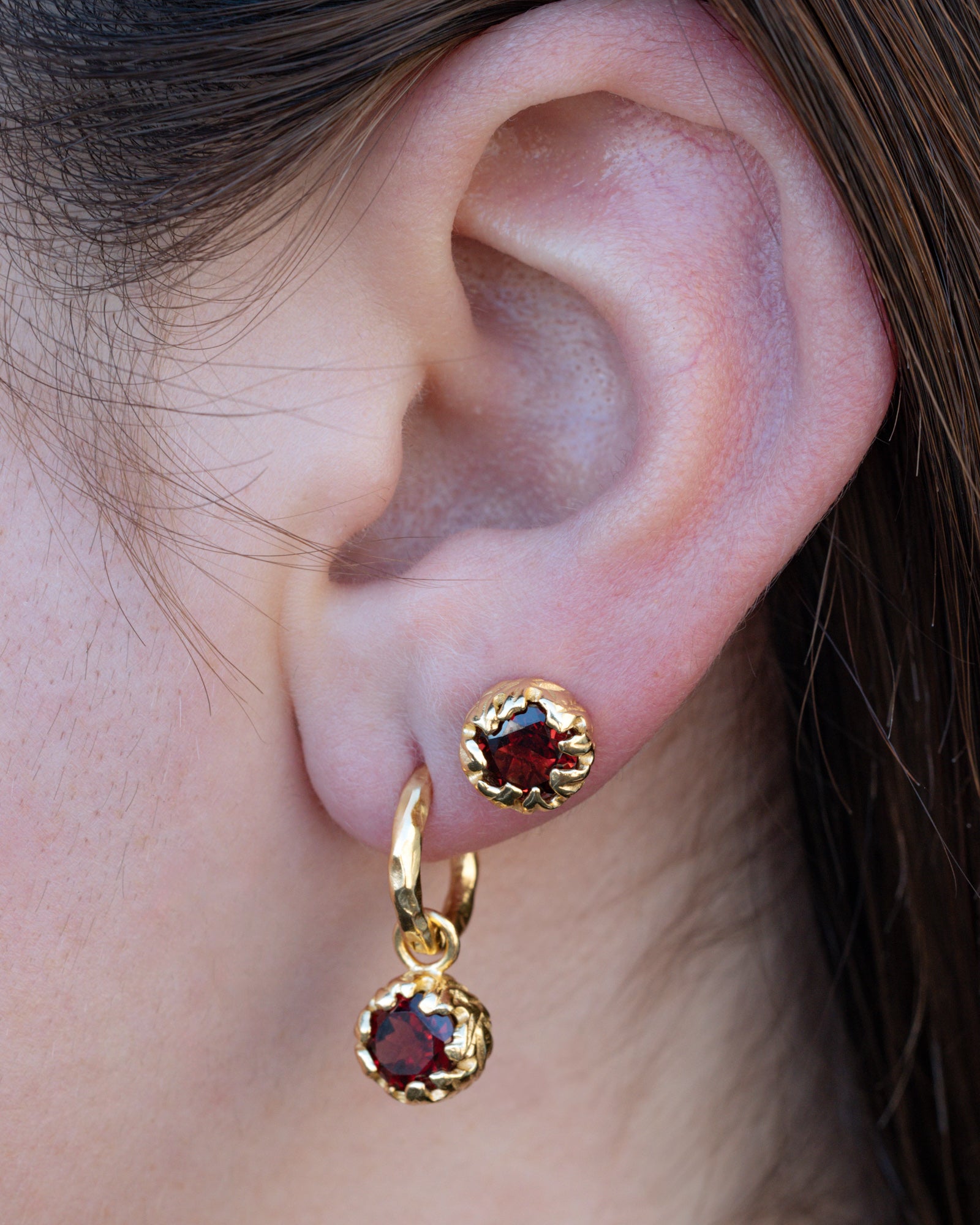 Gold earrings with red garnets worn by a person