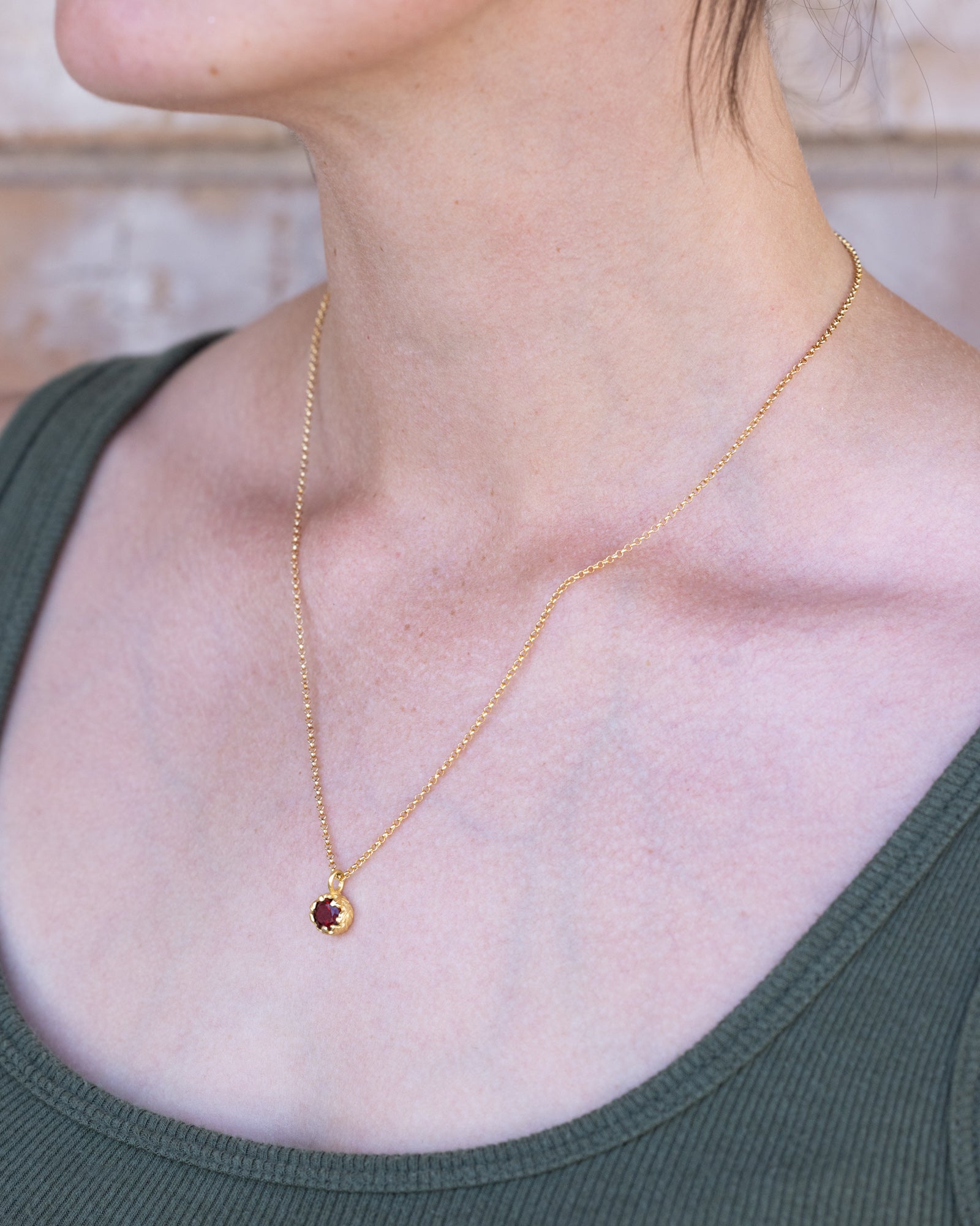 Gold necklace with a red garnet on a person wearing a green top.