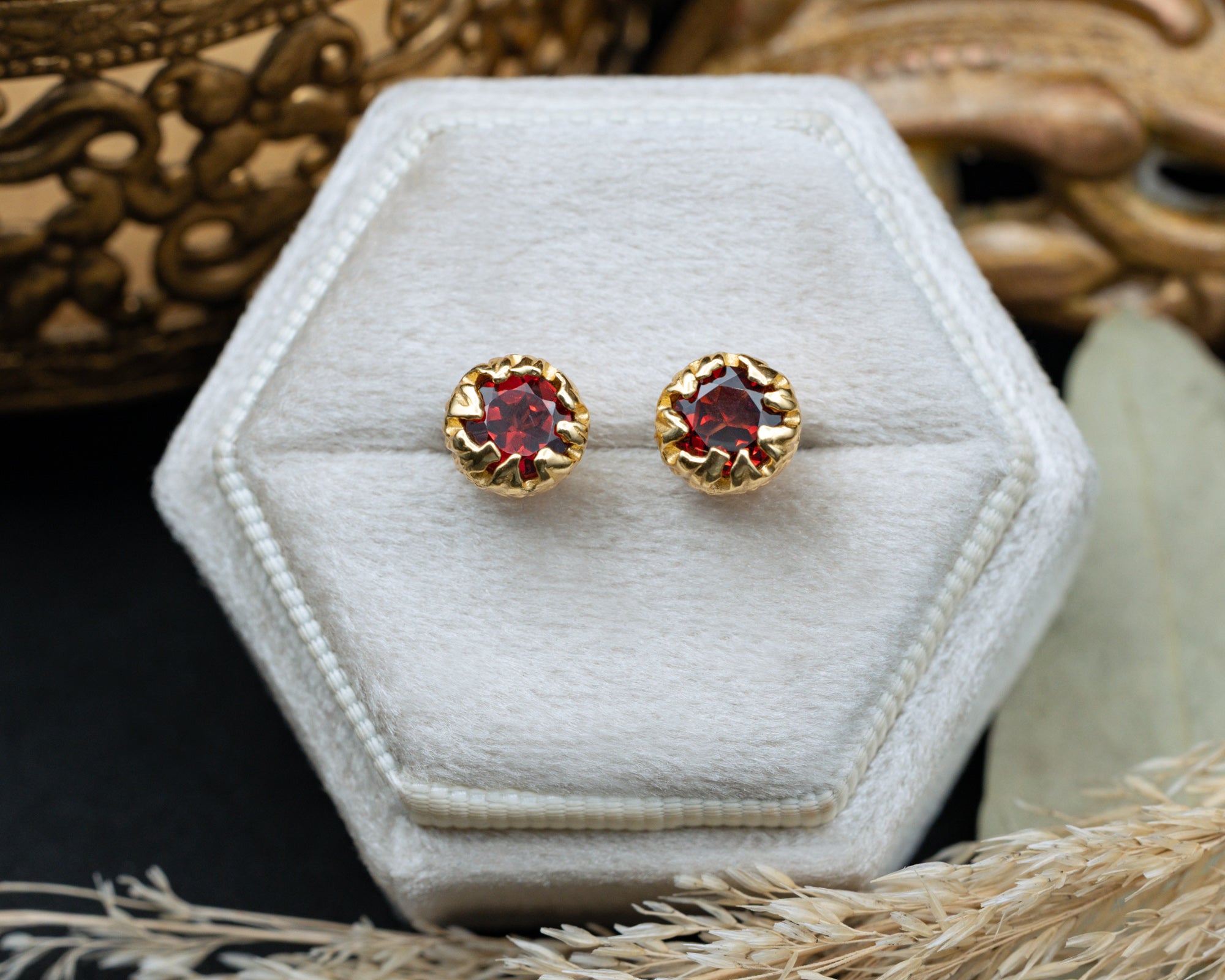 Gold earrings with red garnets on a hexagonal white pillow.