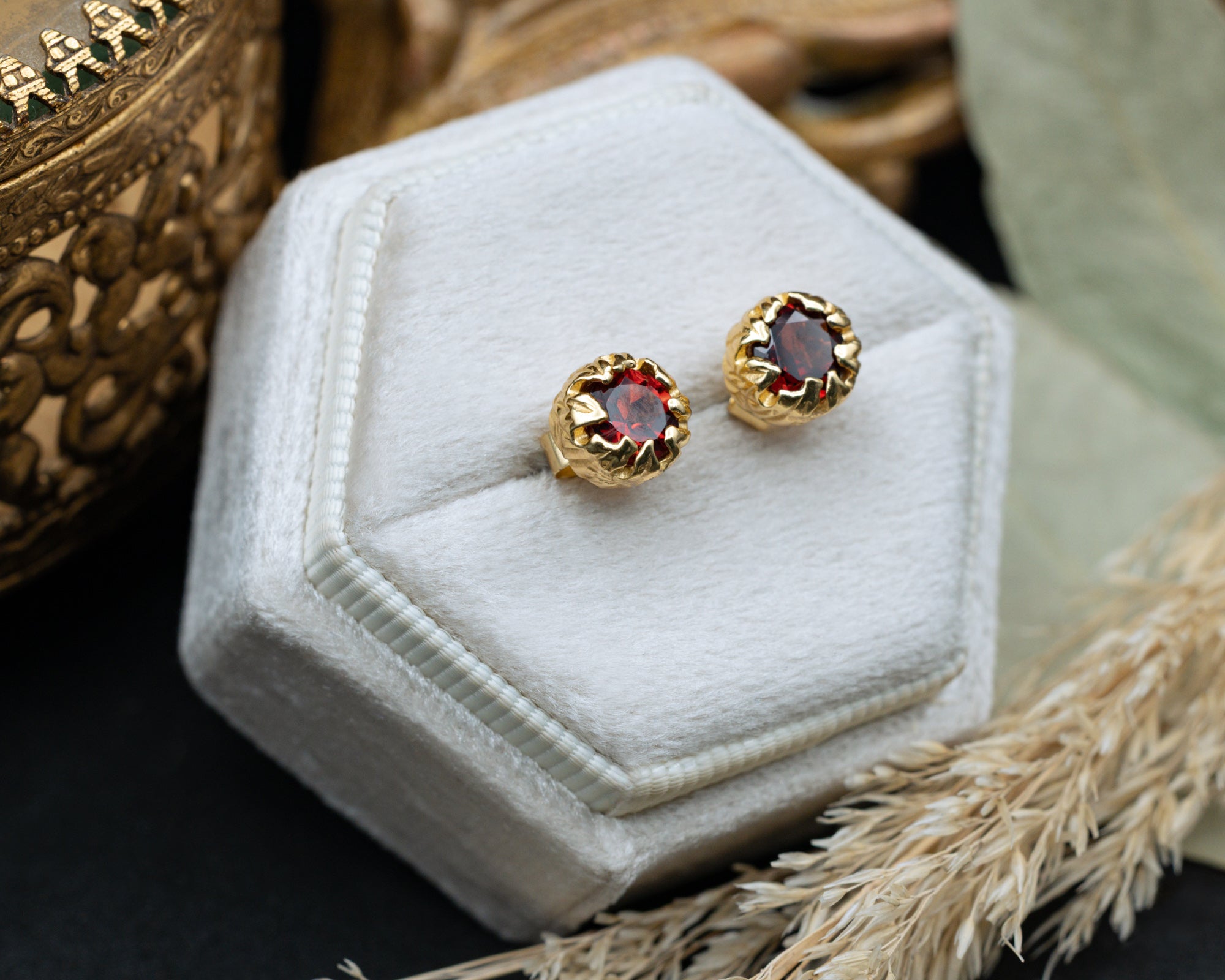 Gold earrings with red garnets on a white velvet stand.